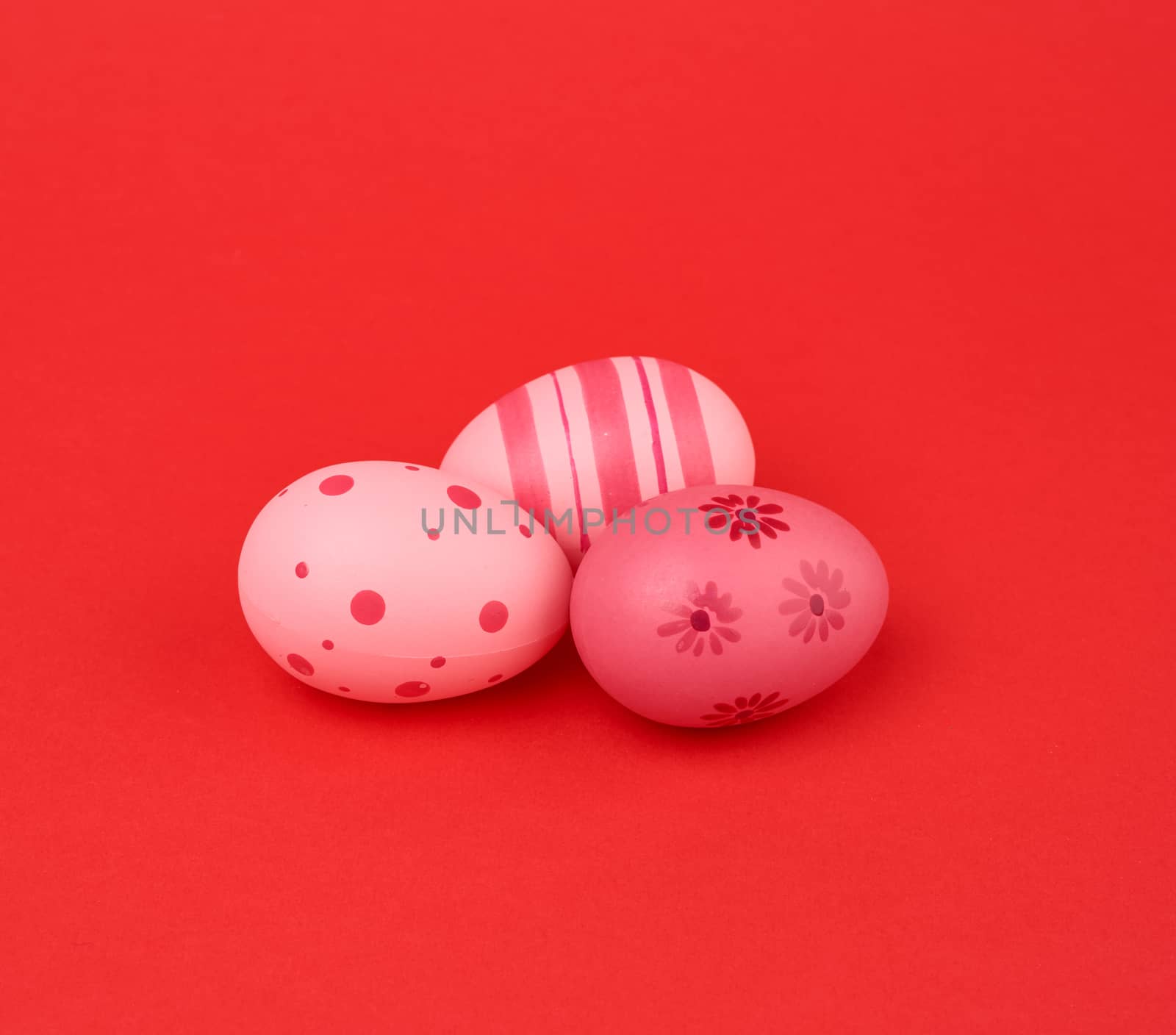 three colored pink easter eggs on a red background, close up