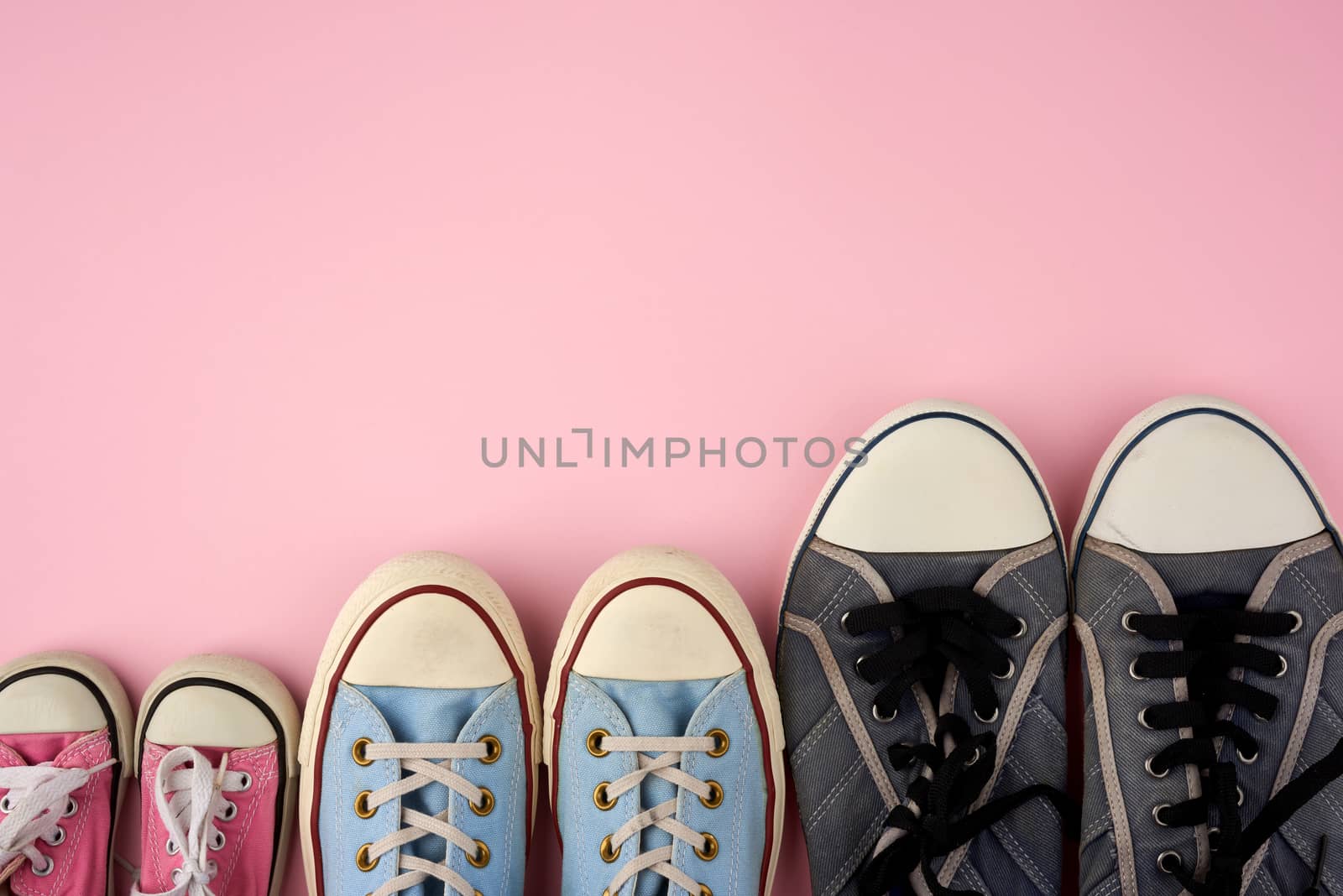 lot of textile worn sneakers of different sizes on a pink background, empty space, family concept