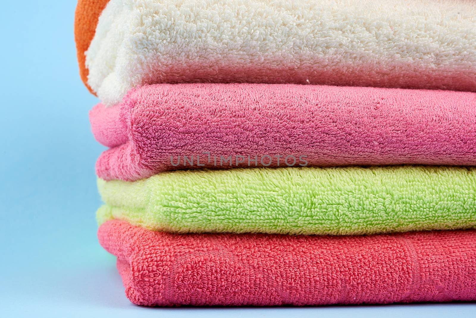 stack of colored cotton terry towels folded against a blue background, close up