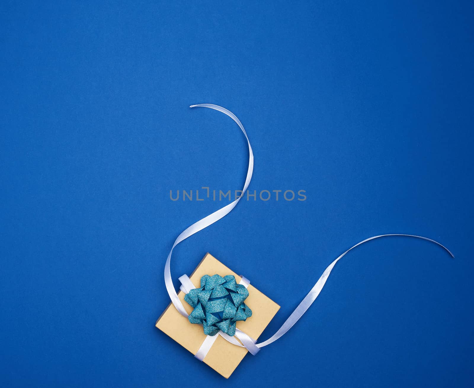 brown square box with a gift tied with a white ribbon with a bow on a blue classic background, top view, empty place for an inscription