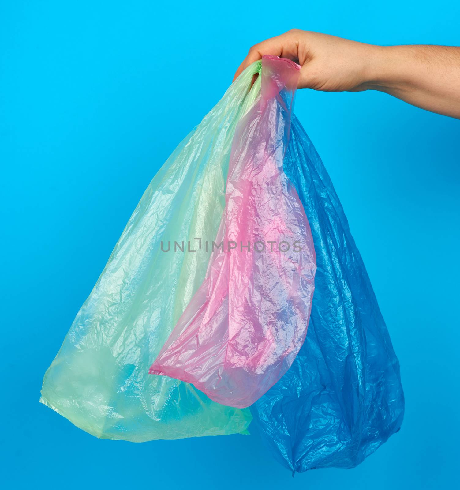hand holds empty multi-colored plastic bags on a blue background, concept of rejection of plastic and the transition to eco-packaging