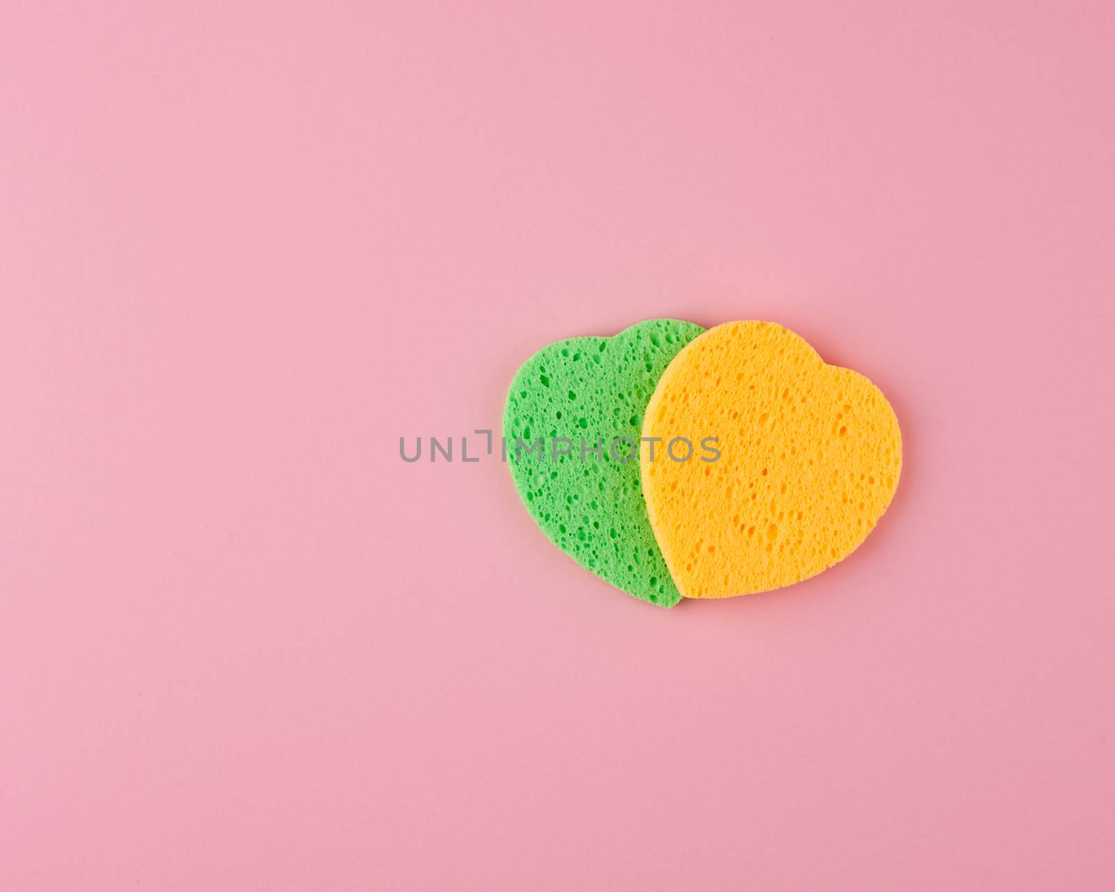 green and yellow heart shaped sponge for face wash on pink background, top view