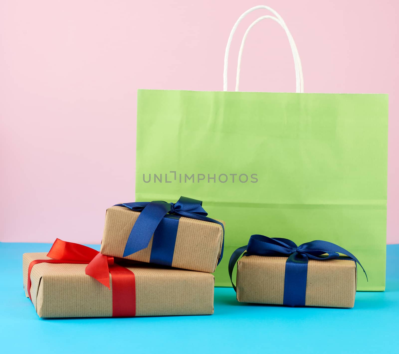 brown paper box with a gift and multi-colored paper bags for shopping and gifts with white handles stand on a pink-blue background