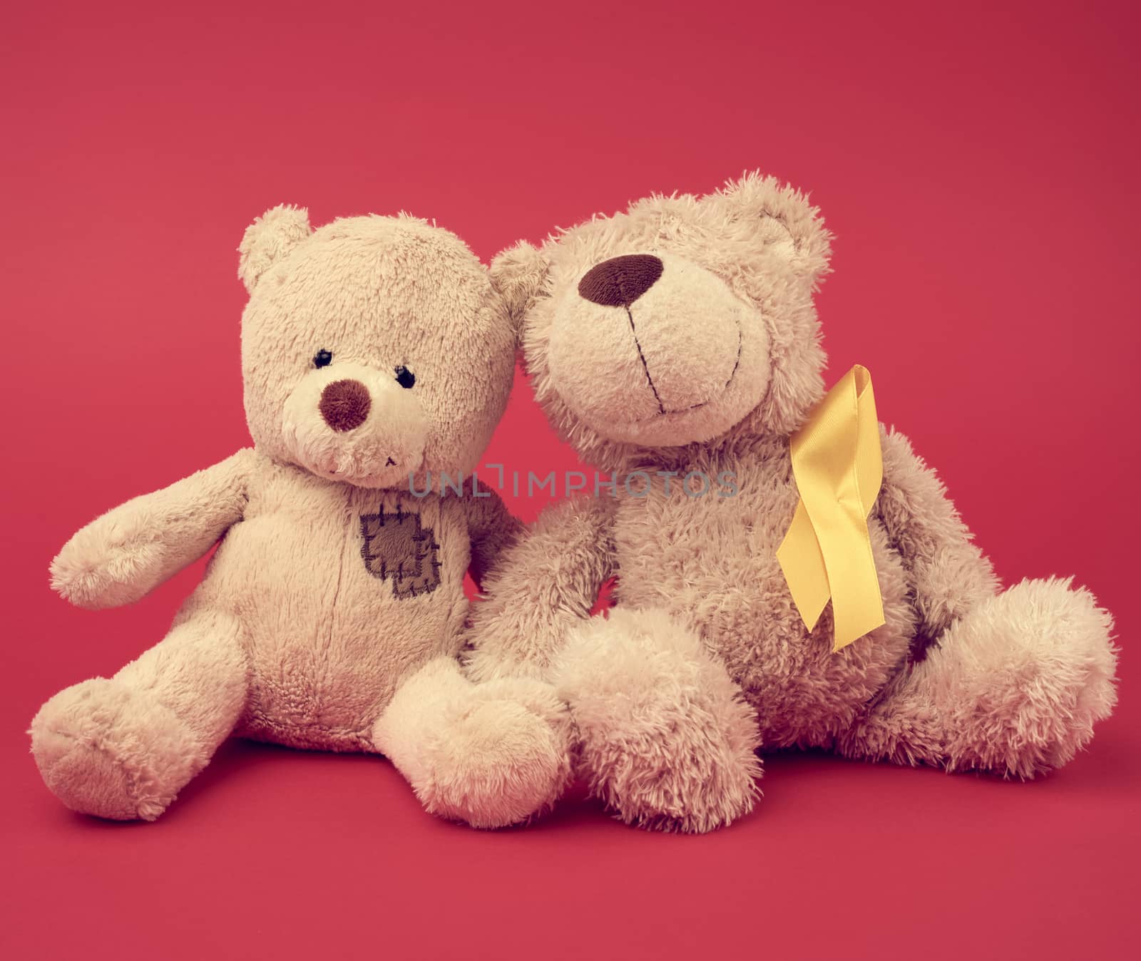 brown teddy bear and a silk yellow ribbon in the shape of a loop on a red background, concept of the fight against childhood cancer, problem of suicides and their prevention