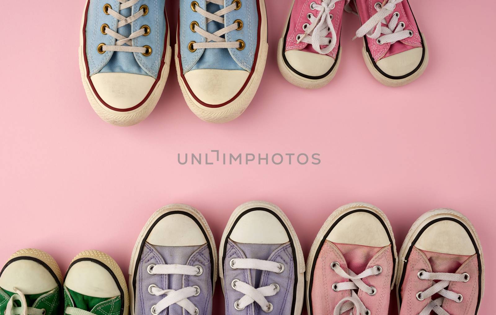 many multi-colored well-worn textile sneakers of different sizes on a pink background, top view, concept, family and team, friendship, copy space