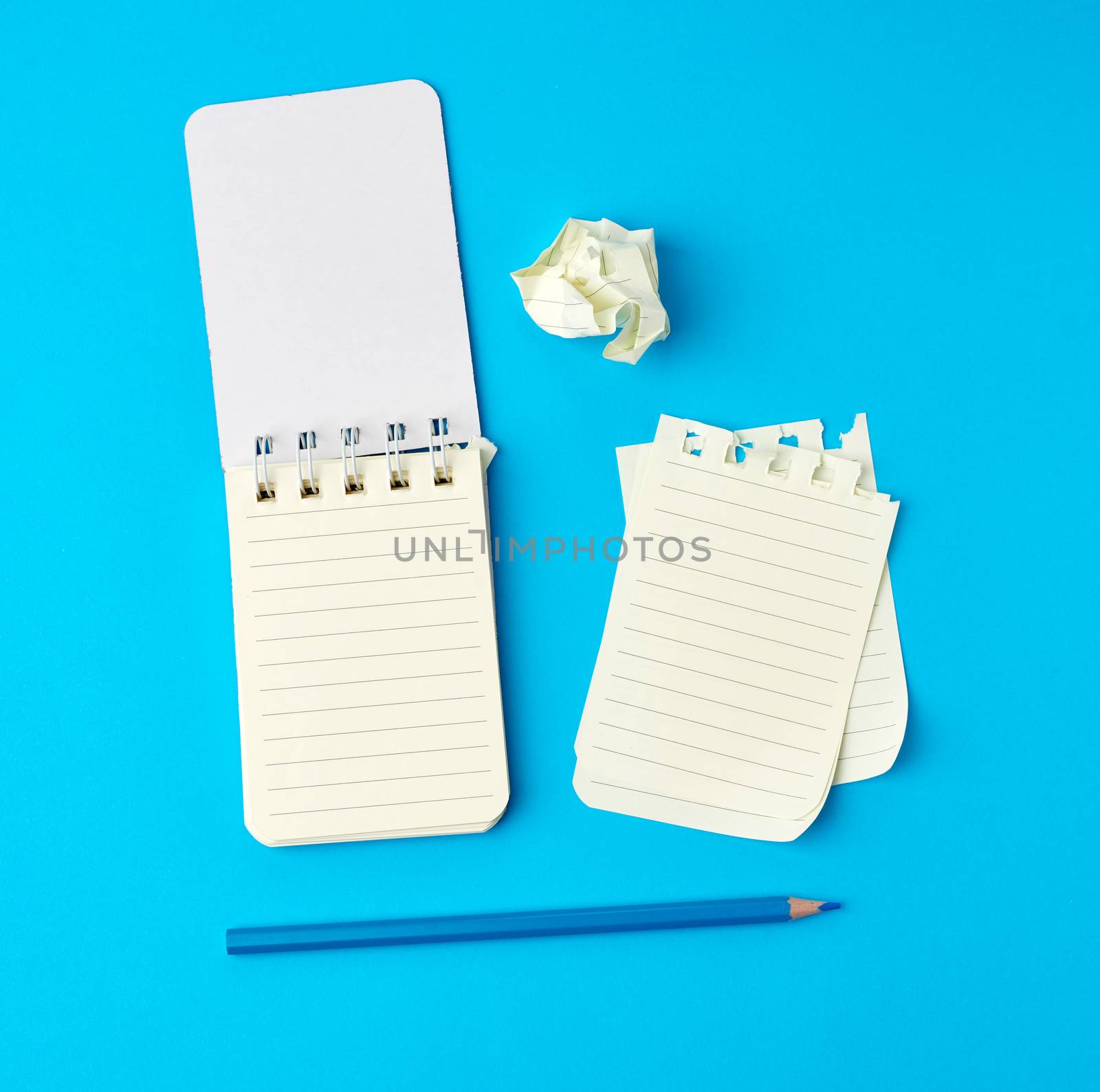 open notebook in line and a blue wooden pencil, next to torn and wrinkled pages, top view