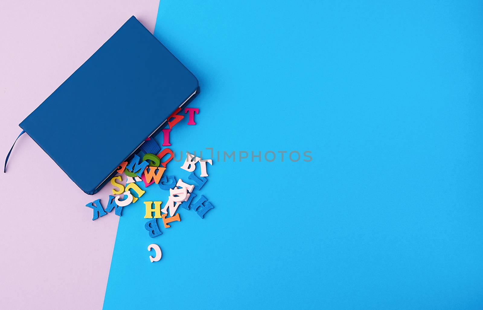 blue notebook and scattered wooden multi-colored letters on an abstract background, top view, flat lay