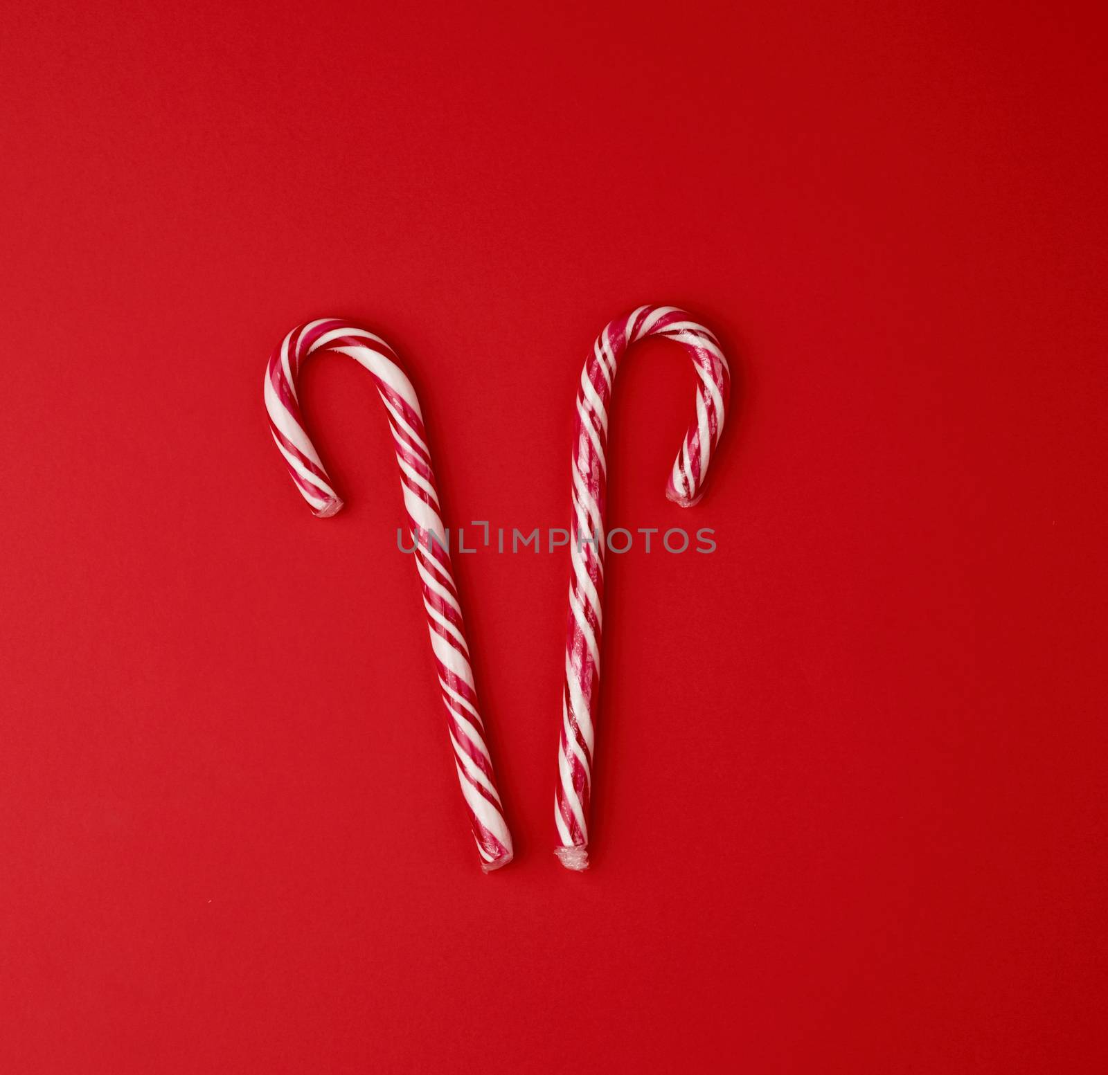 red-white candy stick in transparent cellophane on a red background, close up