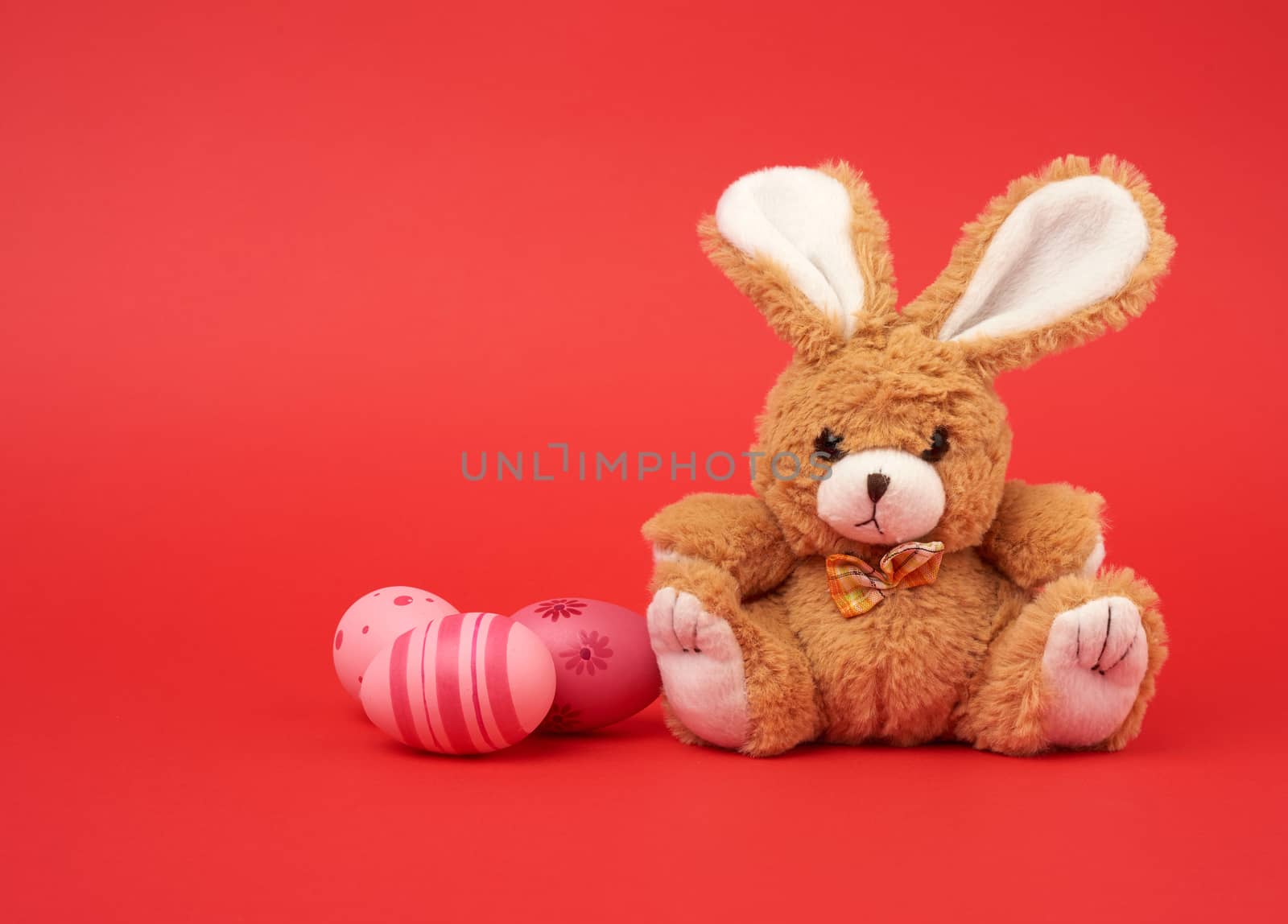 cute brown bunny and pink colored eggs on a red background, easter backdrop