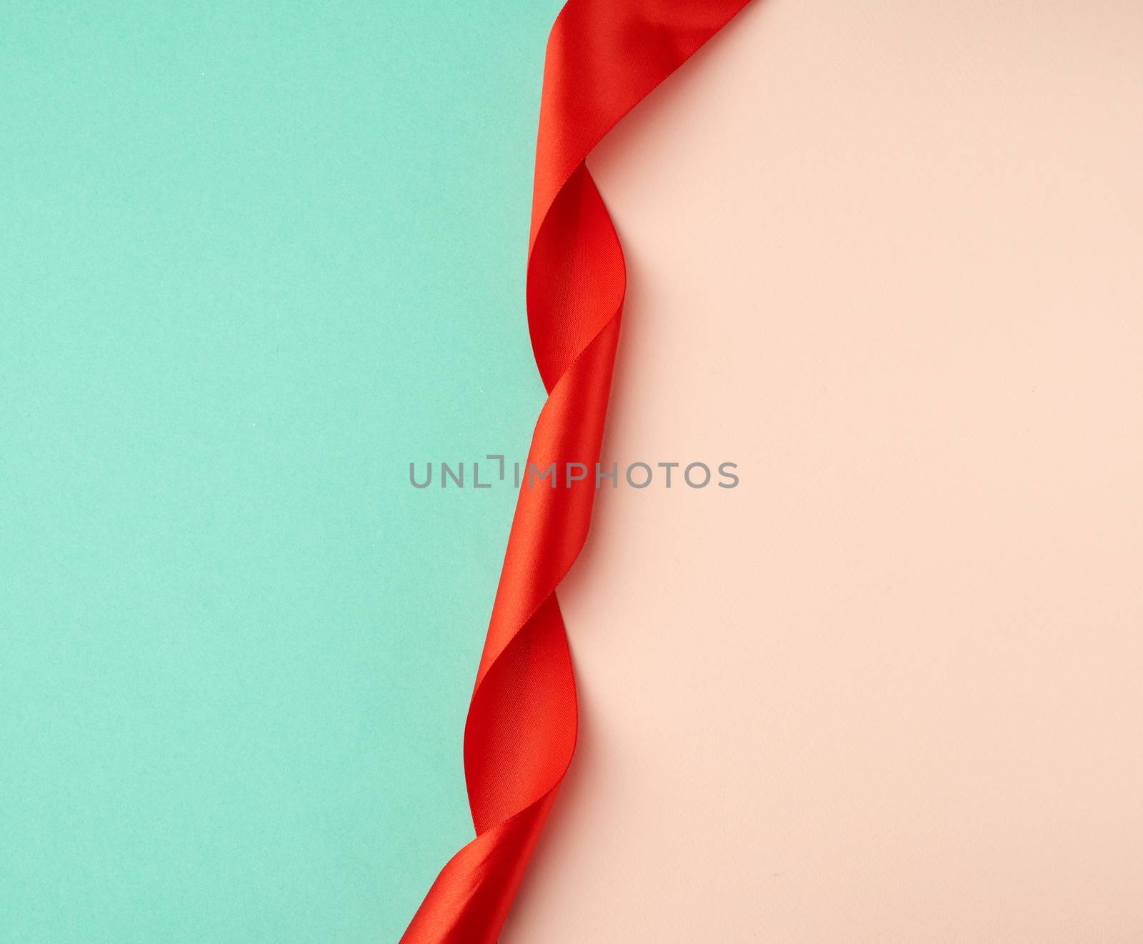 twisted silk red ribbon on a green-beige background, top view