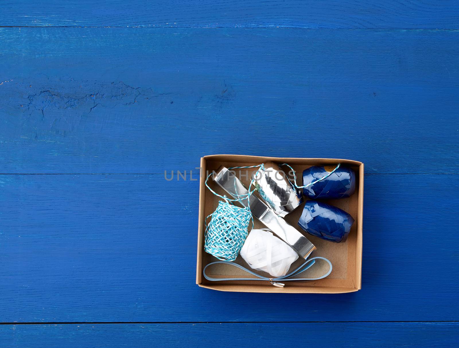 brown cardboard box with a set of decor ribbons for wrapping gifts on a dark blue background, top view