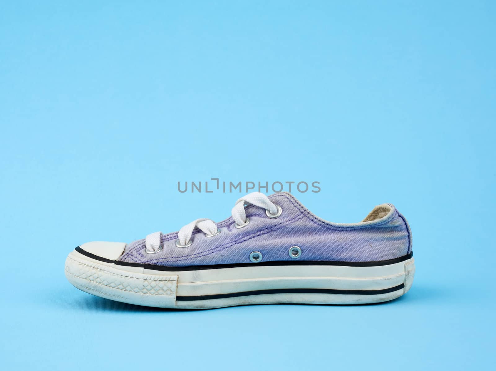 purple worn textile sneaker with white laces on a light blue background, side view of shoes