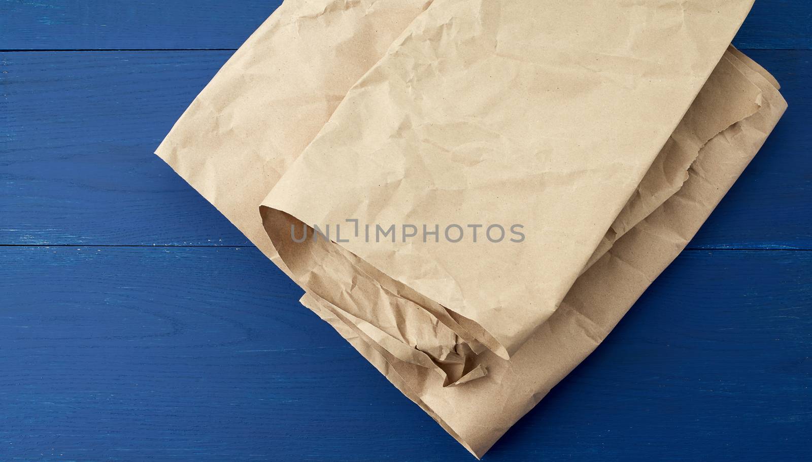 folded brown crumpled kraft paper sheet on blue wooden background, close up