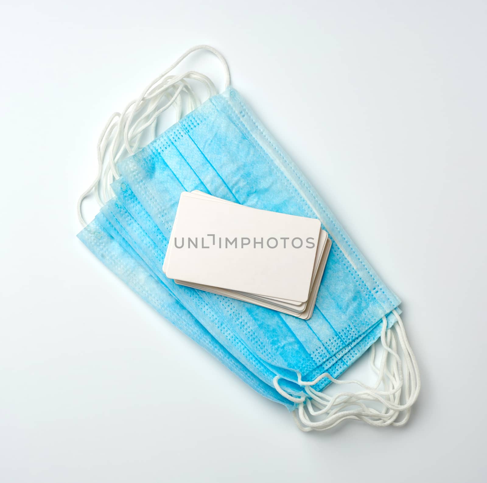 stack of disposable blue medical masks and rectangular blank paper business cards on a white background, top view