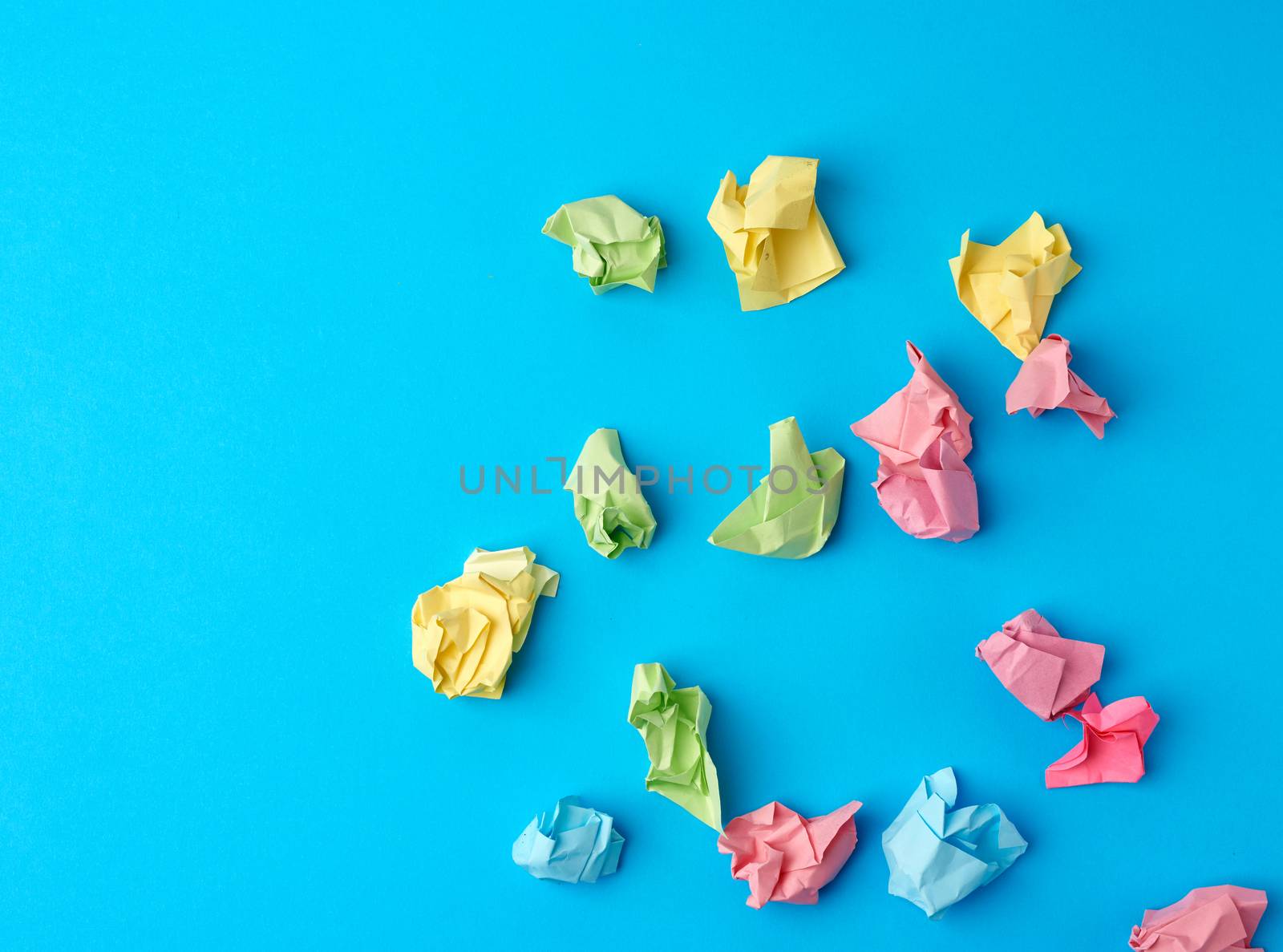 crumpled multi-colored paper stickers, top view, blue background