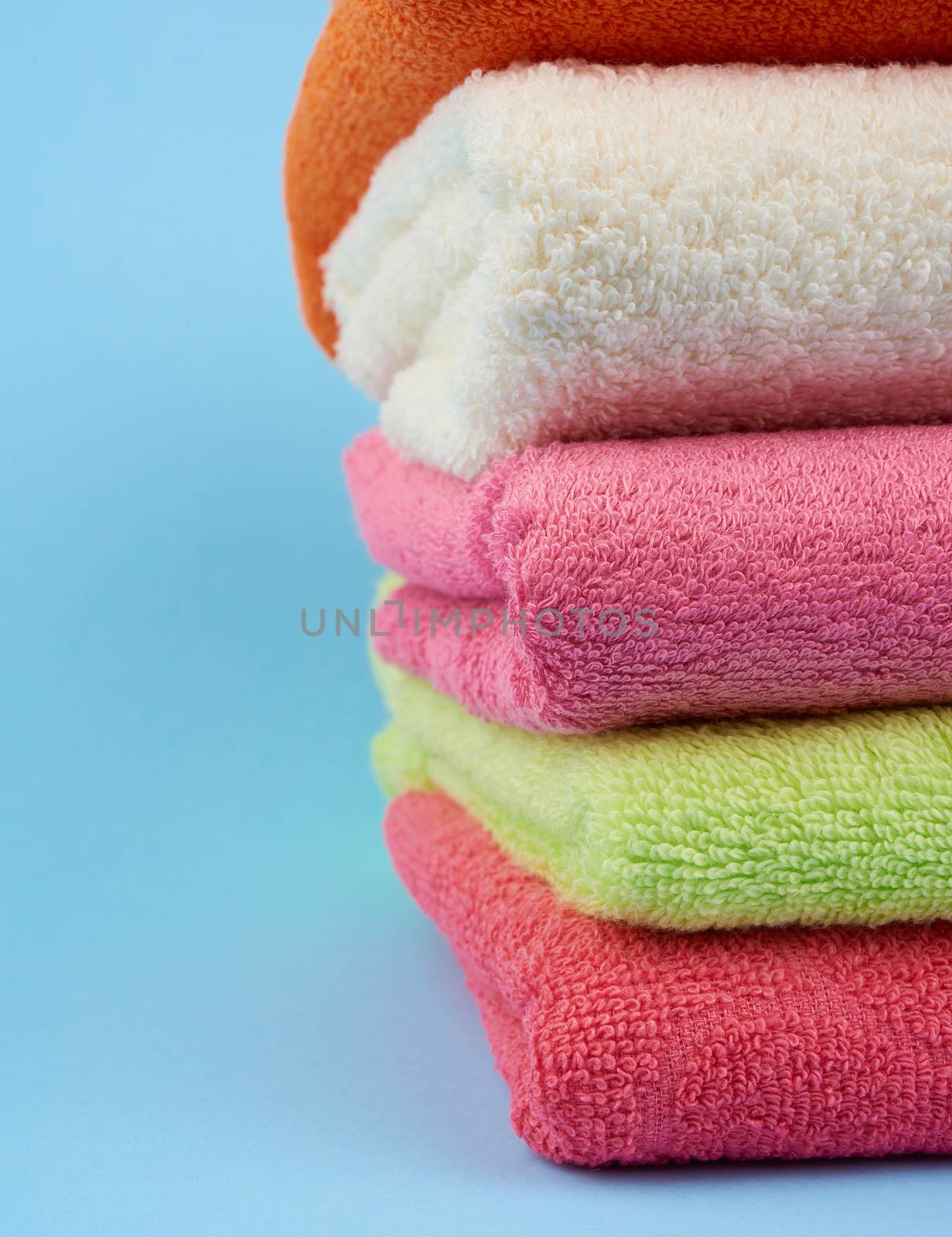 stack of colored cotton terry folded towels on a blue background by ndanko