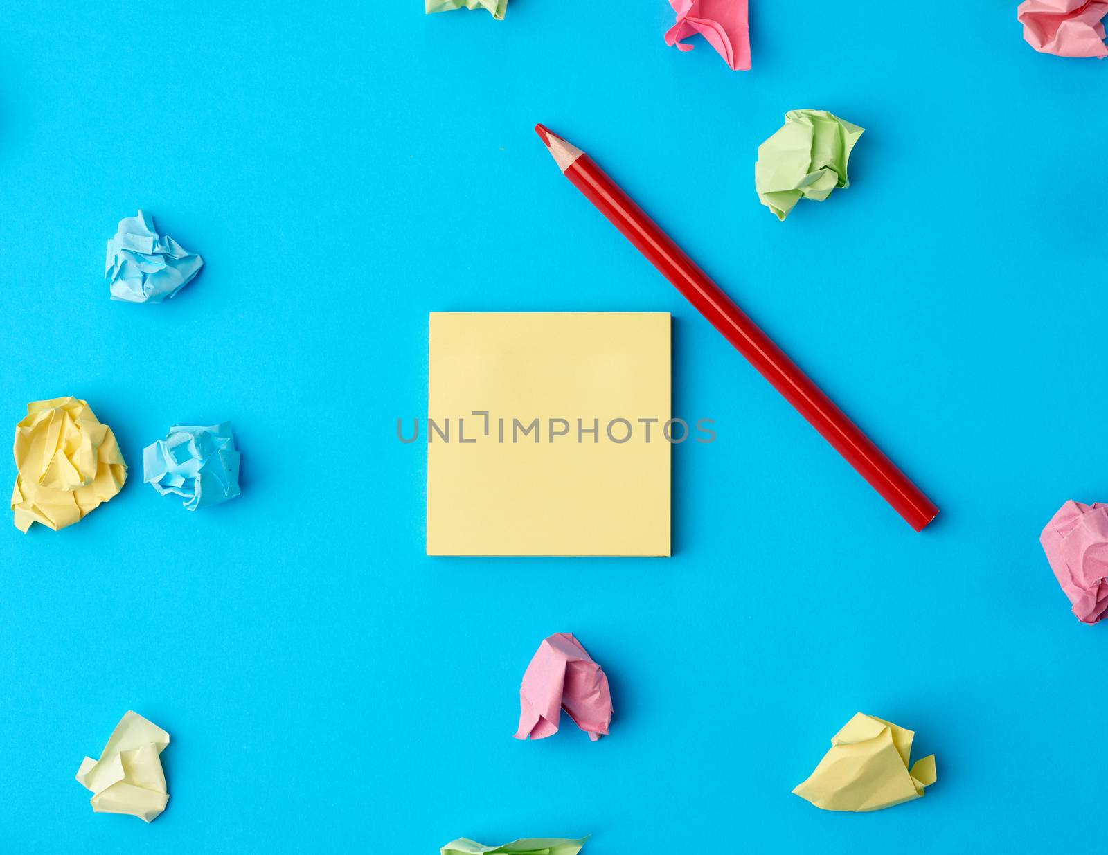 multicolored blank paper stickers of different colors and wooden pencil on a blue background, copy space