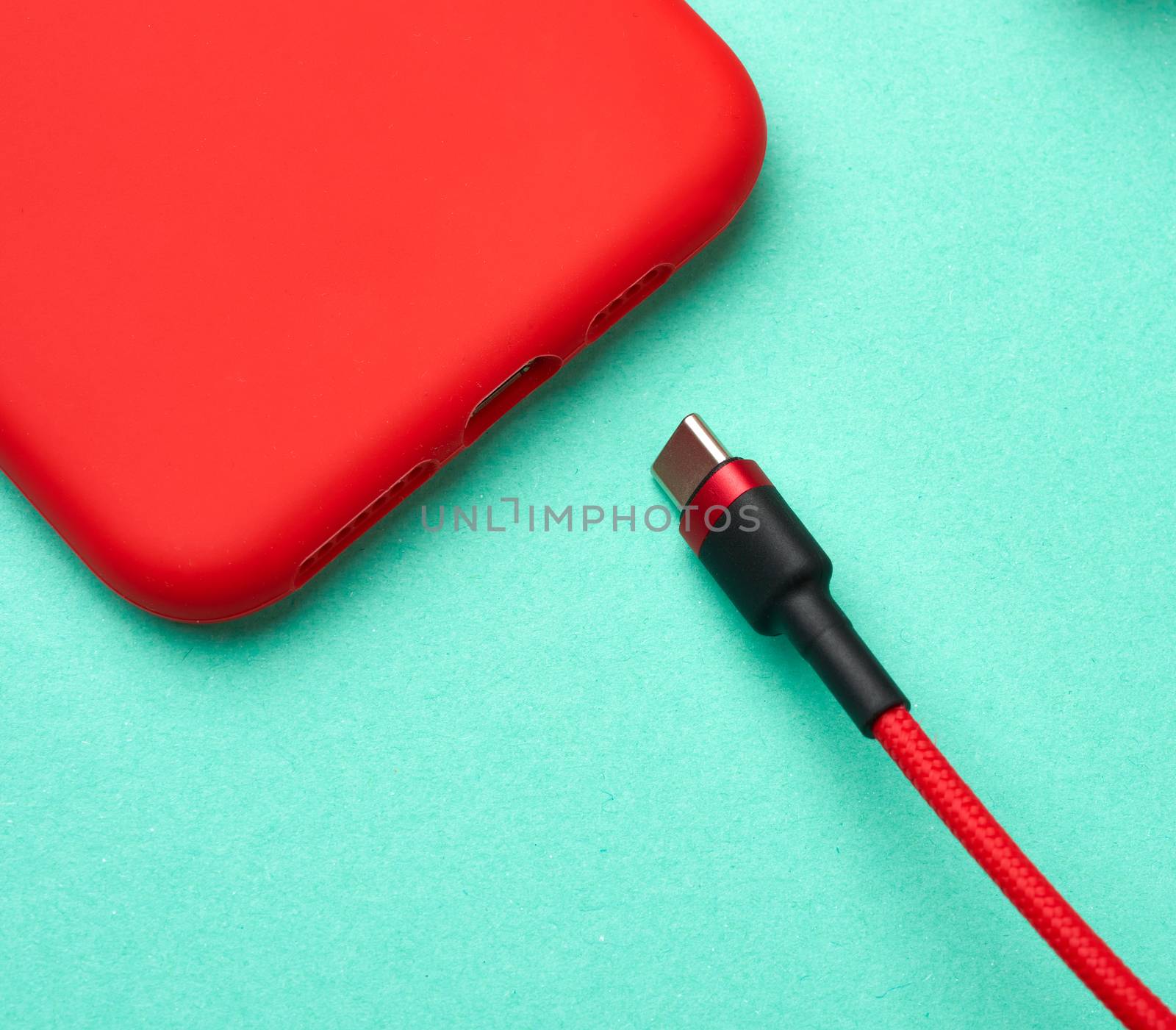 red smartphone and cable in textile braid on a green background, close up