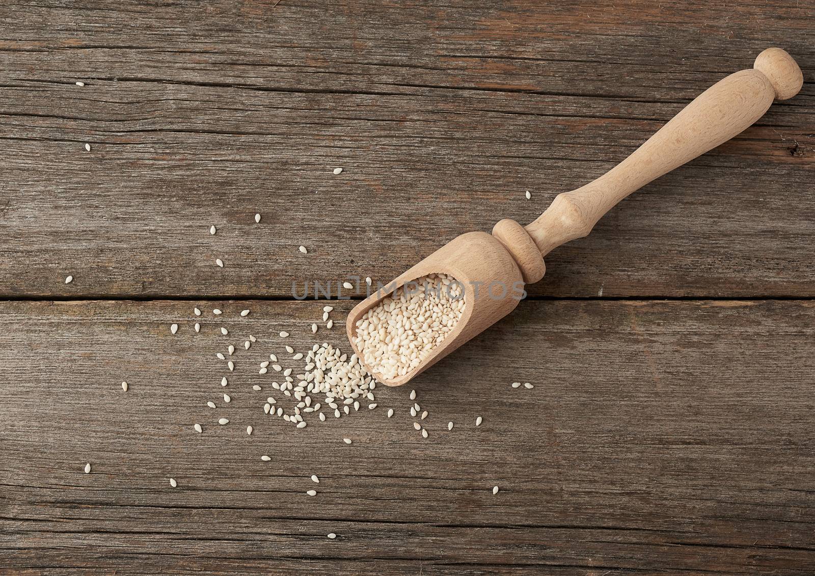 dry white sesame seeds in a brown wooden spoon on a gray wooden table from old boards, top view