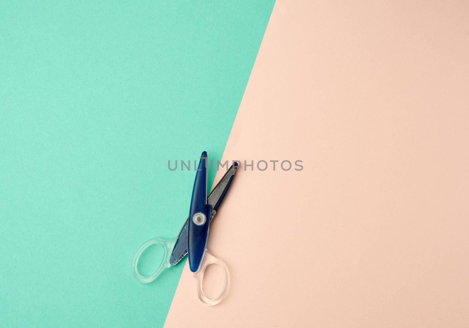 blue plastic paper scissors on a green-beige background, top view, flat lay