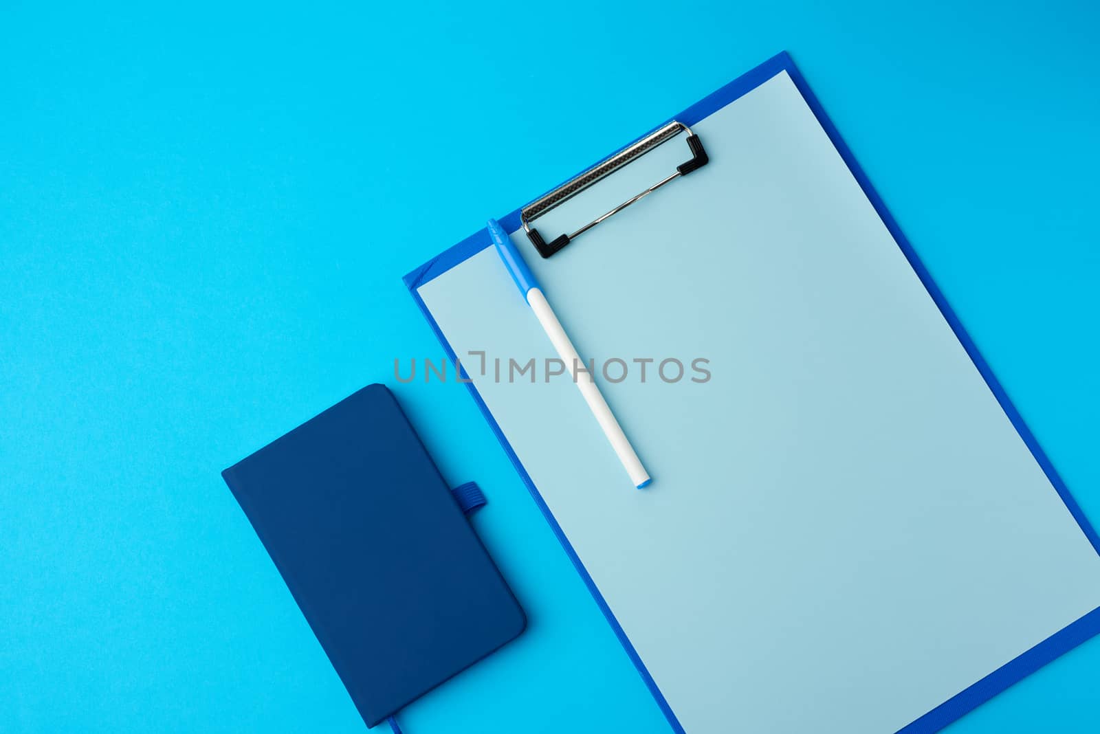 blue holder with empty sheets and notebook on a blue background, copy space