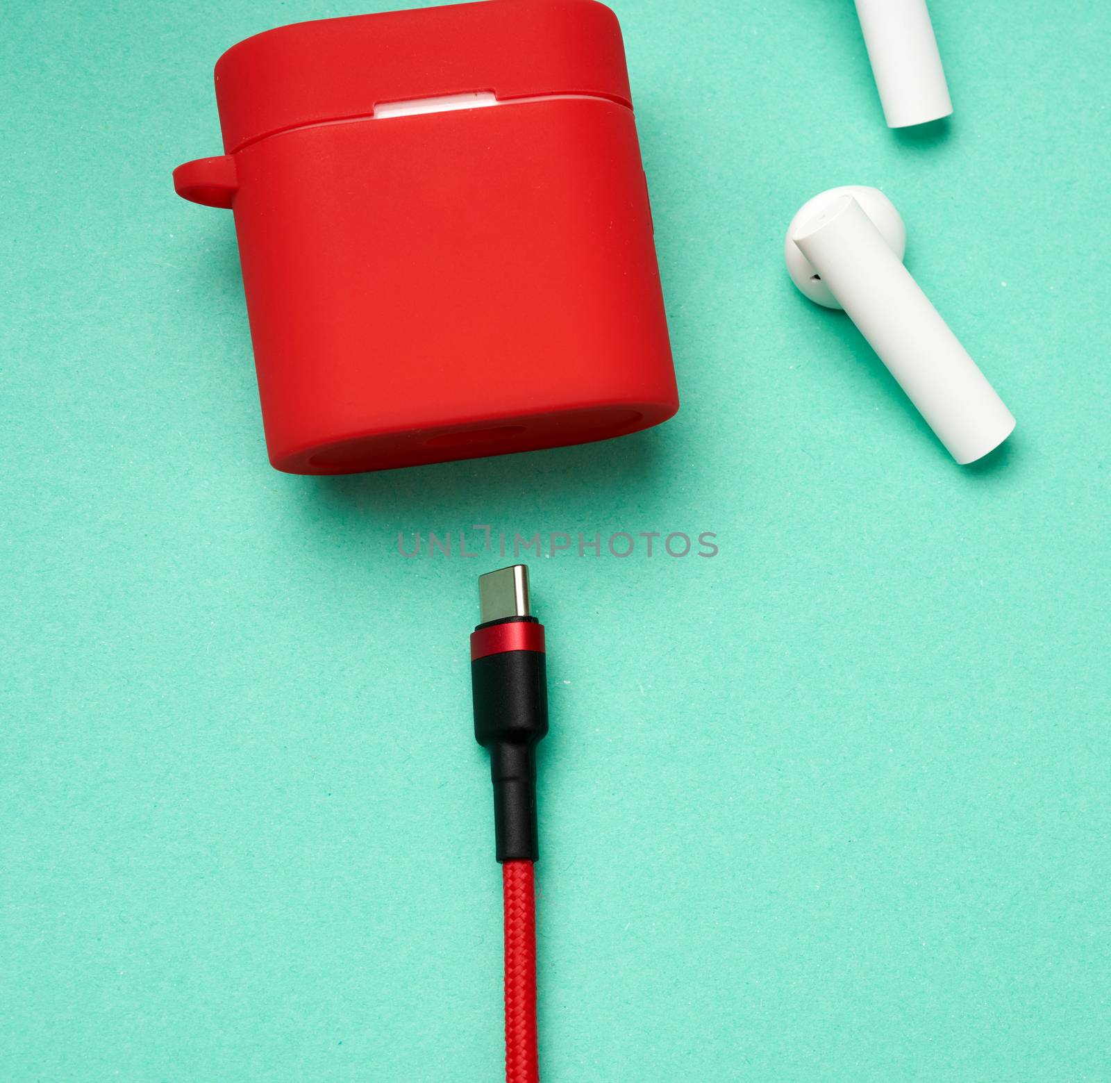 red charging box and sticks headphones on a green background, close up, wireless device