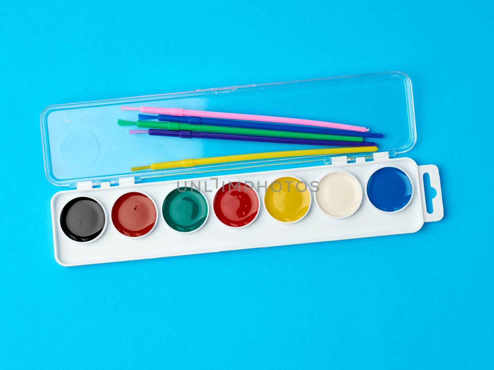 multicolored watercolor paints in a plastic box and brushes on a blue background, set for drawing, close up