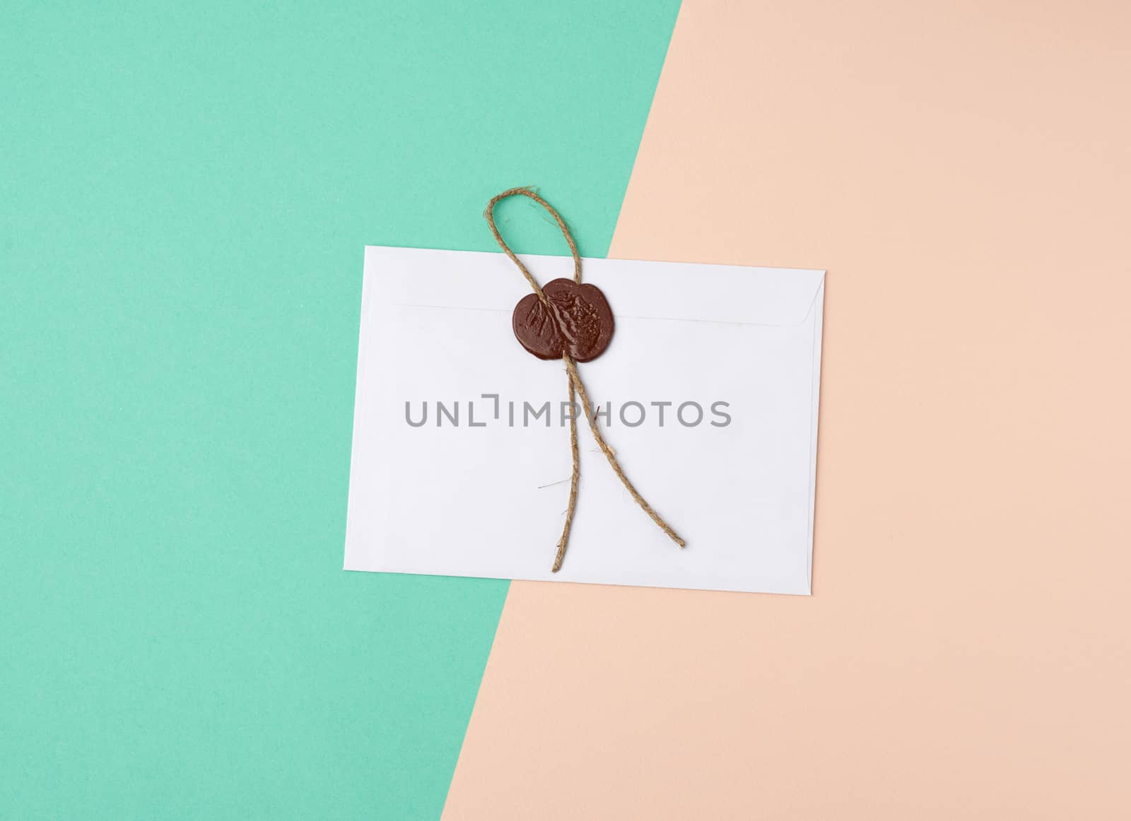 rectangular white paper envelope and brown stamp, color background, flat lay