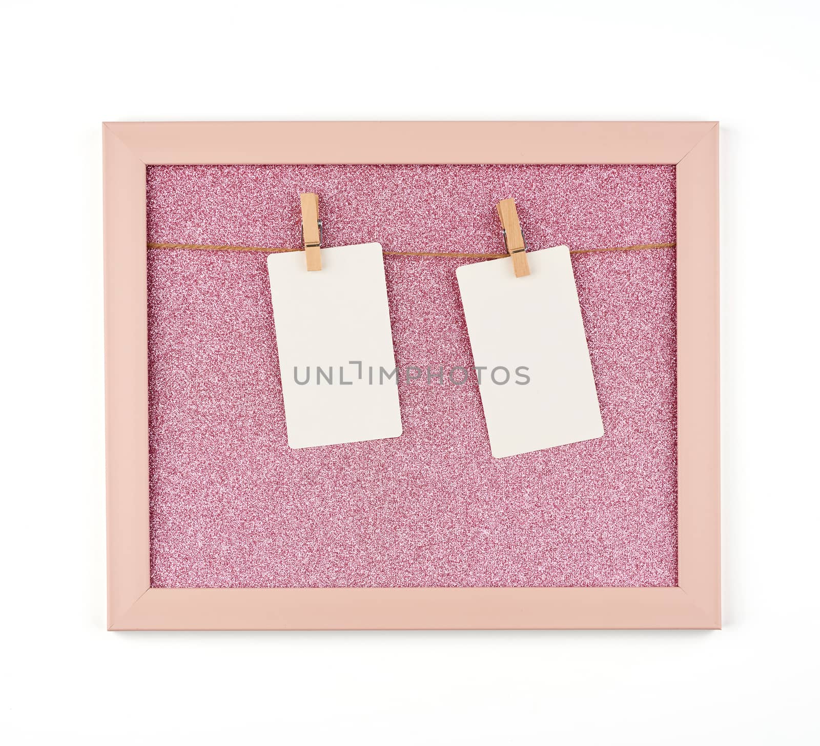 pink shiny frame with ropes and empty white paper sheets hanging on wooden clothespins, place for photo and inscription