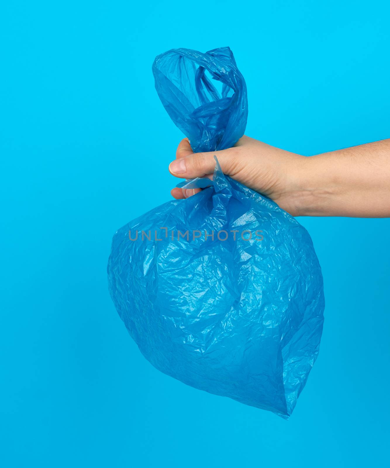 hand holds an empty blue plastic bag on a blue background by ndanko