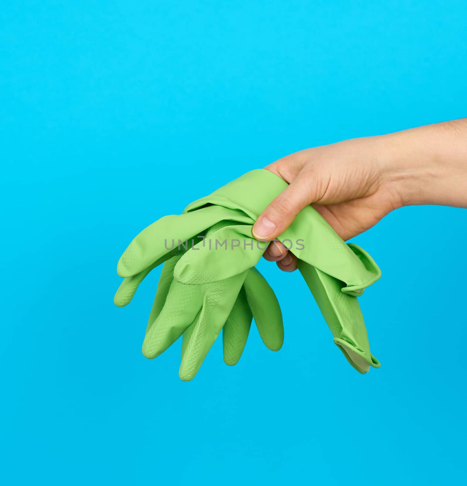 female hand holds green rubber gloves for cleaning, blue background