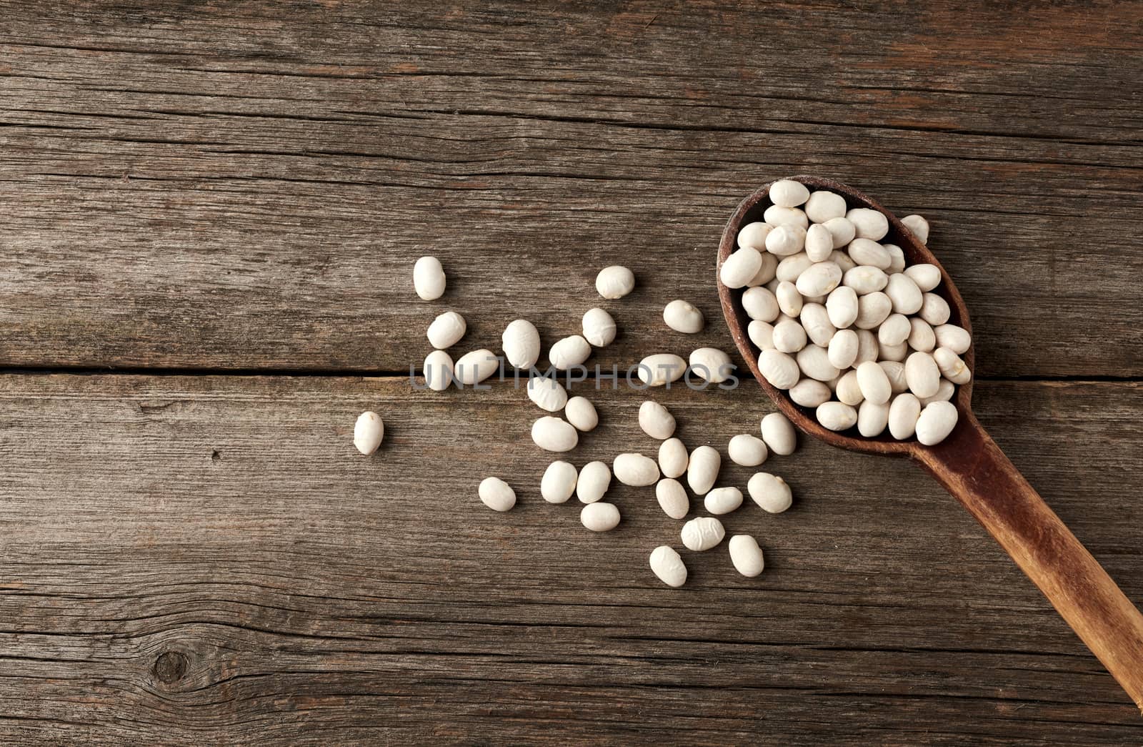 white raw whole beans in a brown wooden spoon on the table, top view