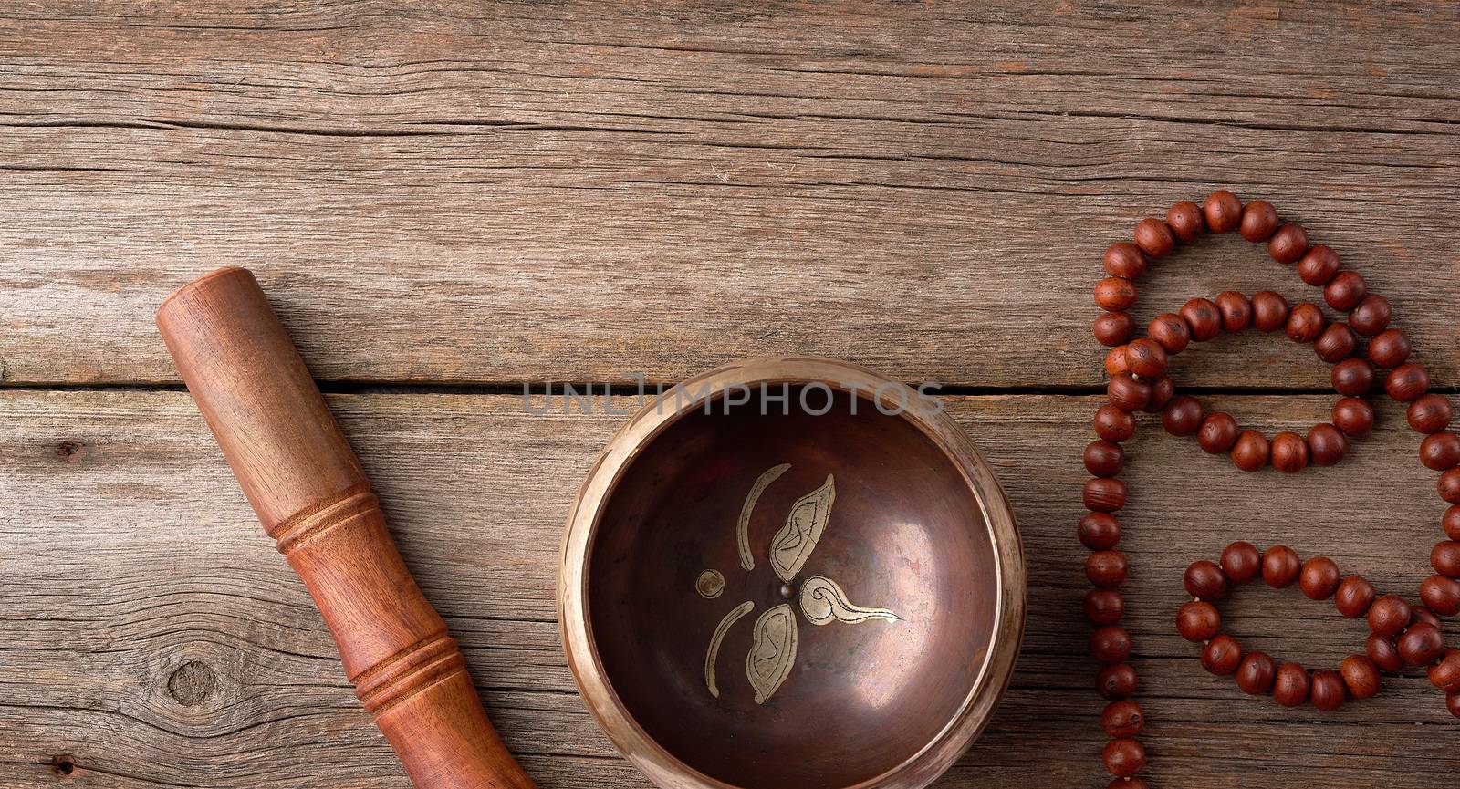 Tibetan singing copper bowl with a wooden clapper and prayer rosary on a gray wooden table, close up