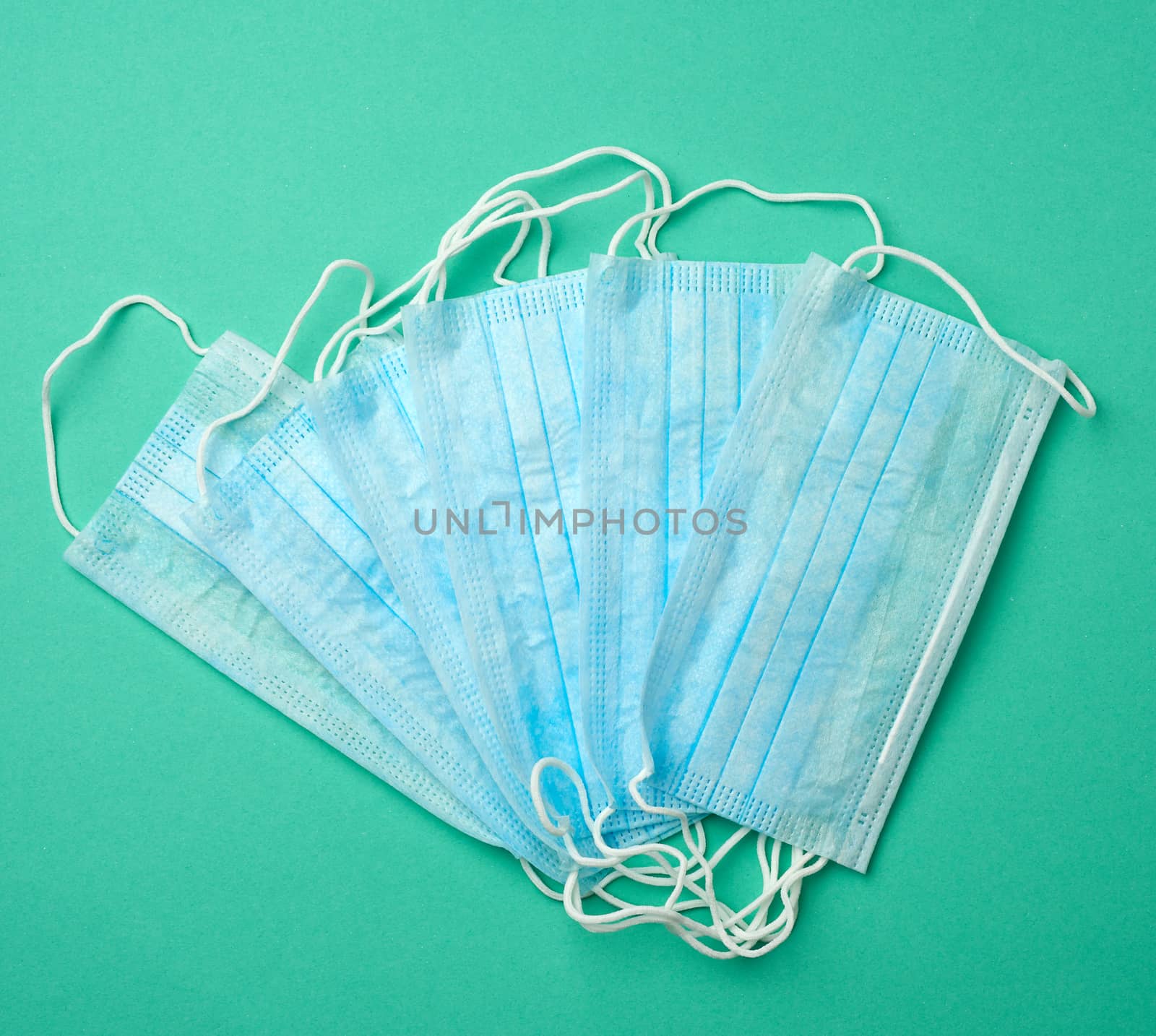 stack of disposable blue medical masks on a green background, top view