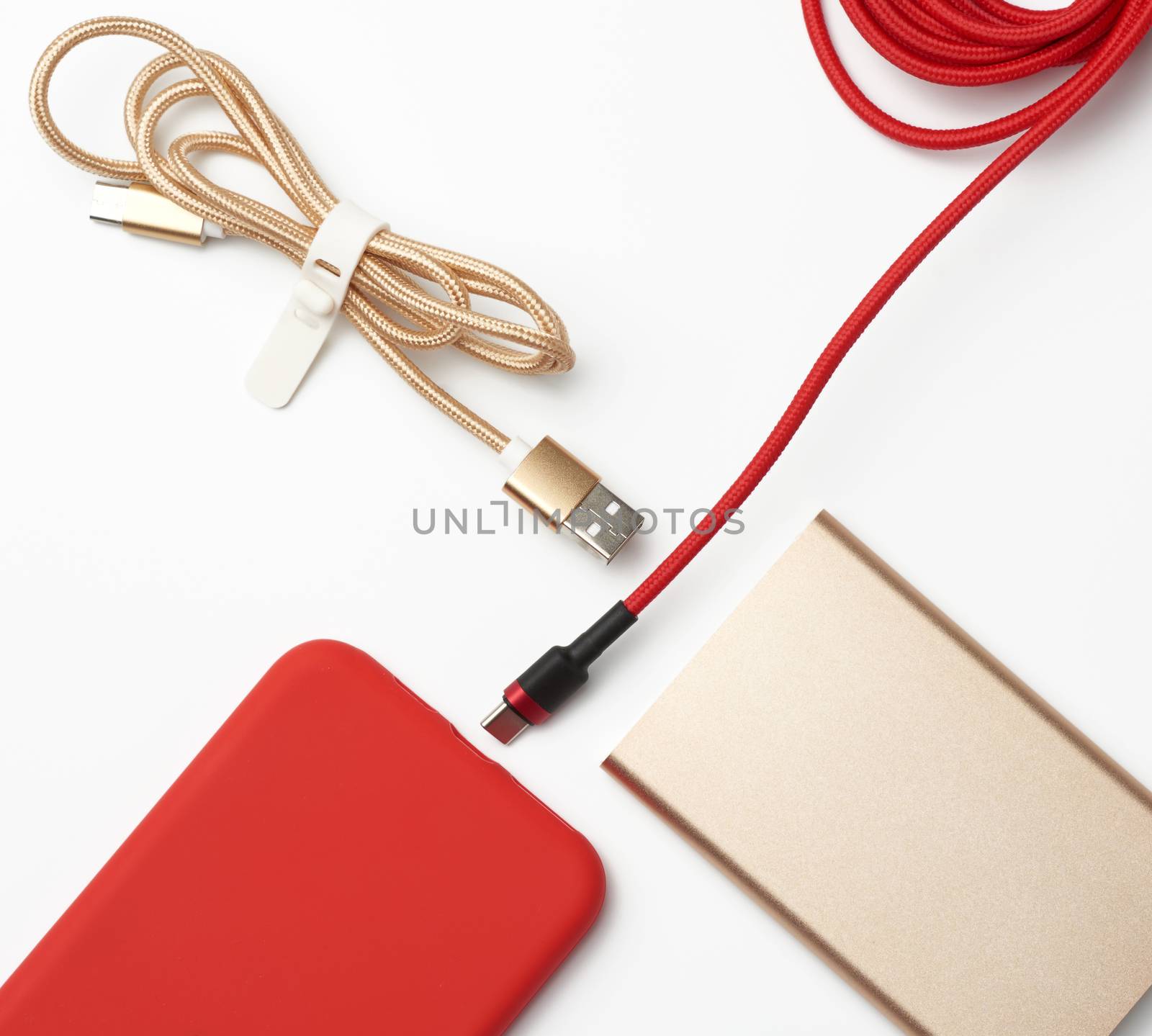 golden power bank, red smartphone and cable in textile braid on a white background, close up, flat lay