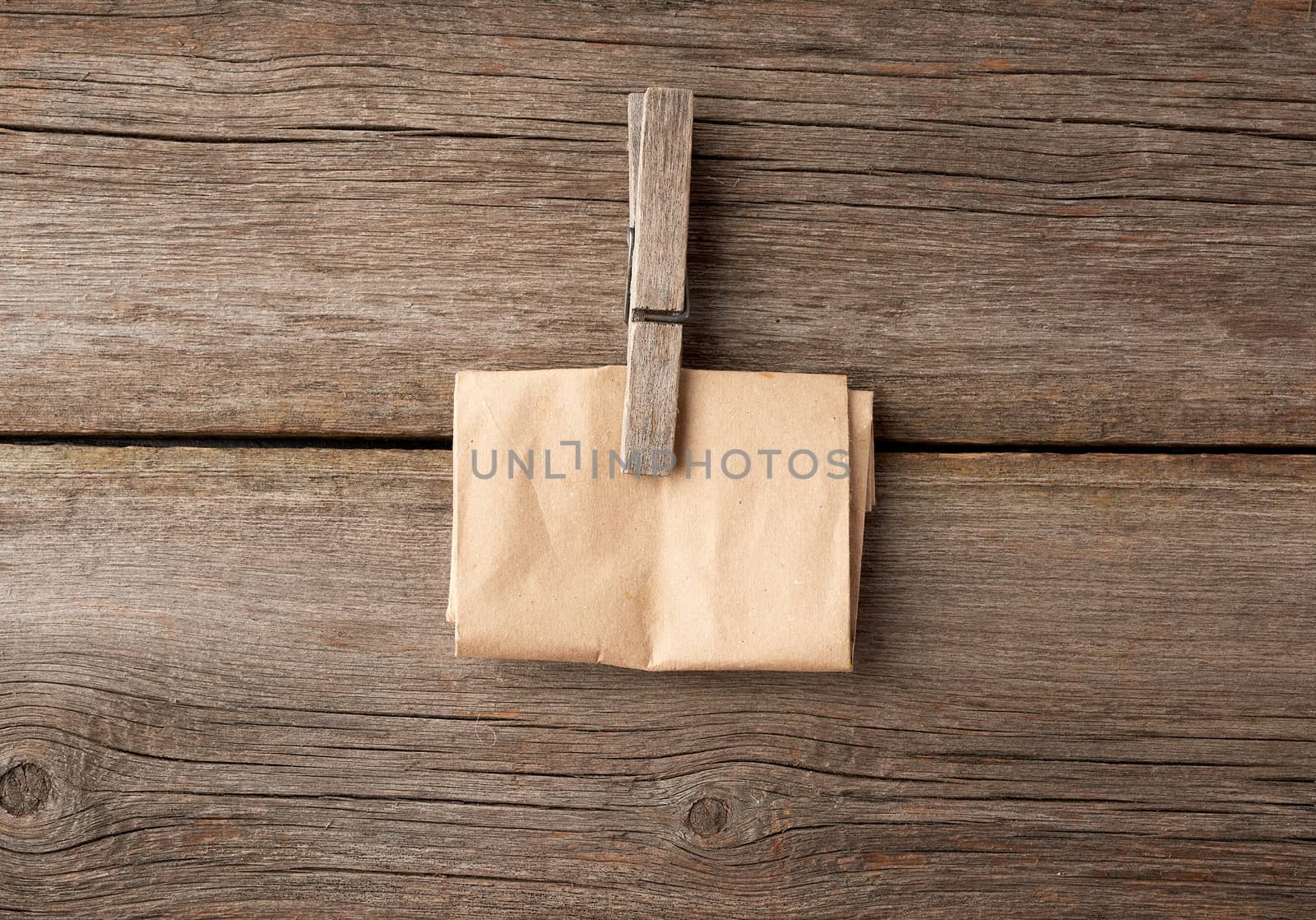 wooden clothespin and folded brown paper on a gray wooden background, close up