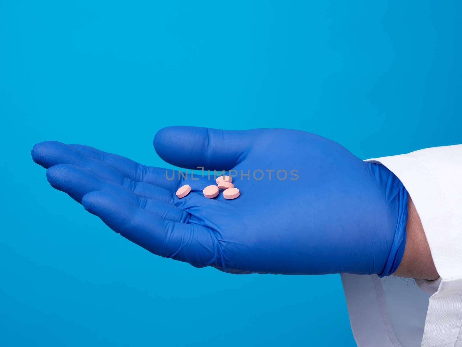 male hand with blue sterile gloves holds round pink pills, concept of drug treatment for diseases, blue background