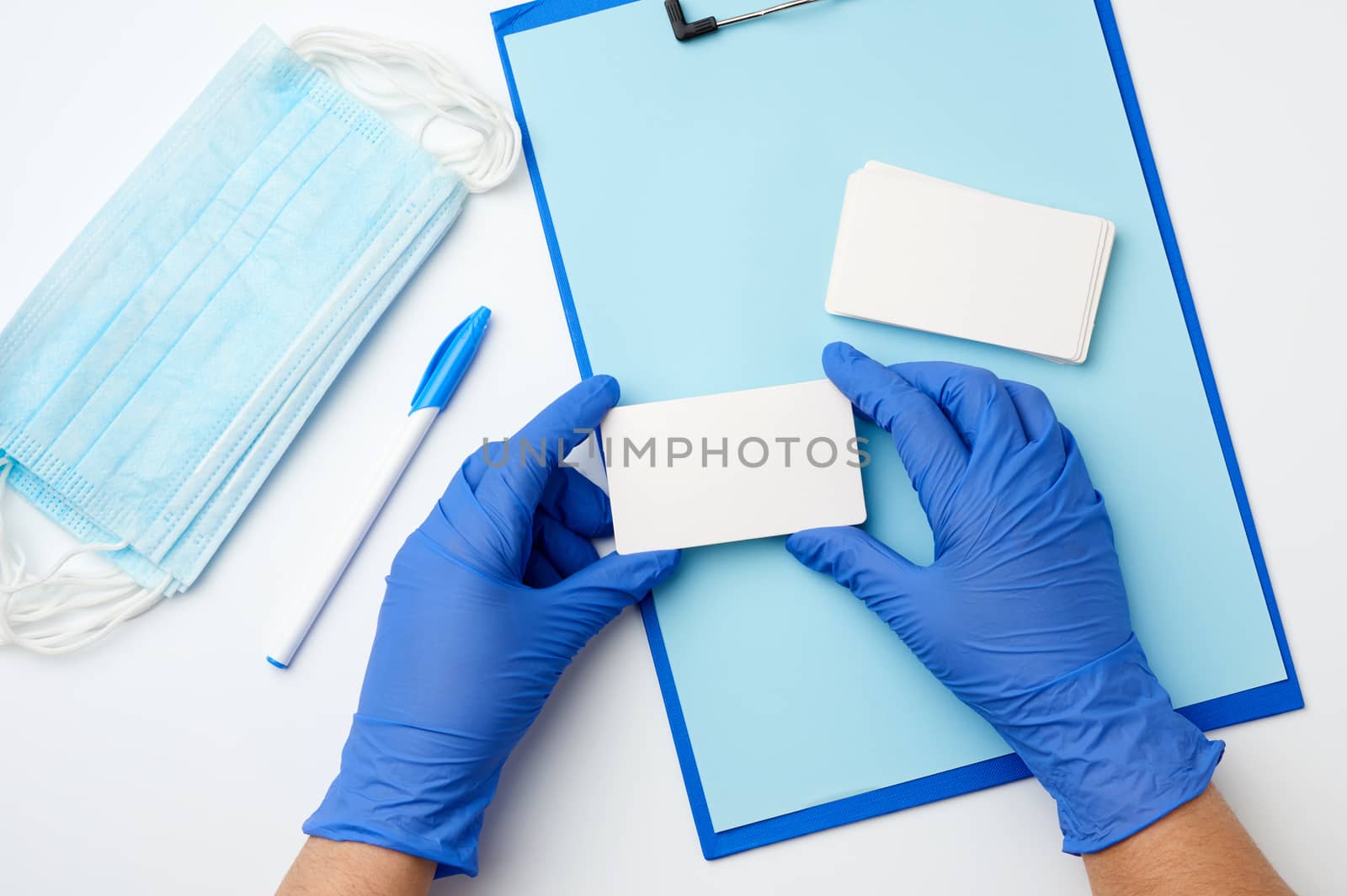 two hands in blue medical gloves are holding rectangular white blank business cards, top view, white background