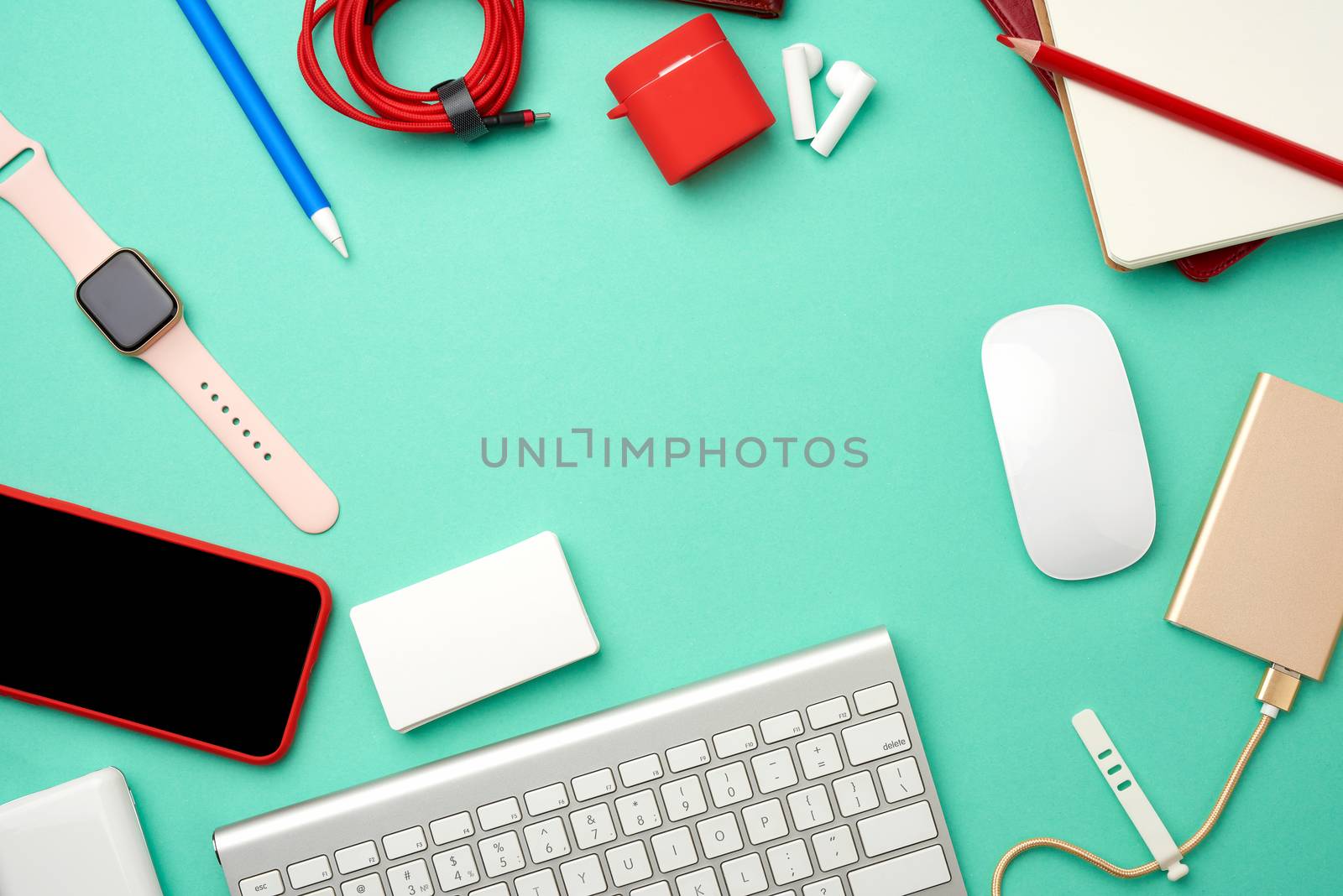 keyboard, golden power bank with cable, red smartphone with blank black screen, headphones, blank paper business cards and wireless mouse on green background, workplace, top view