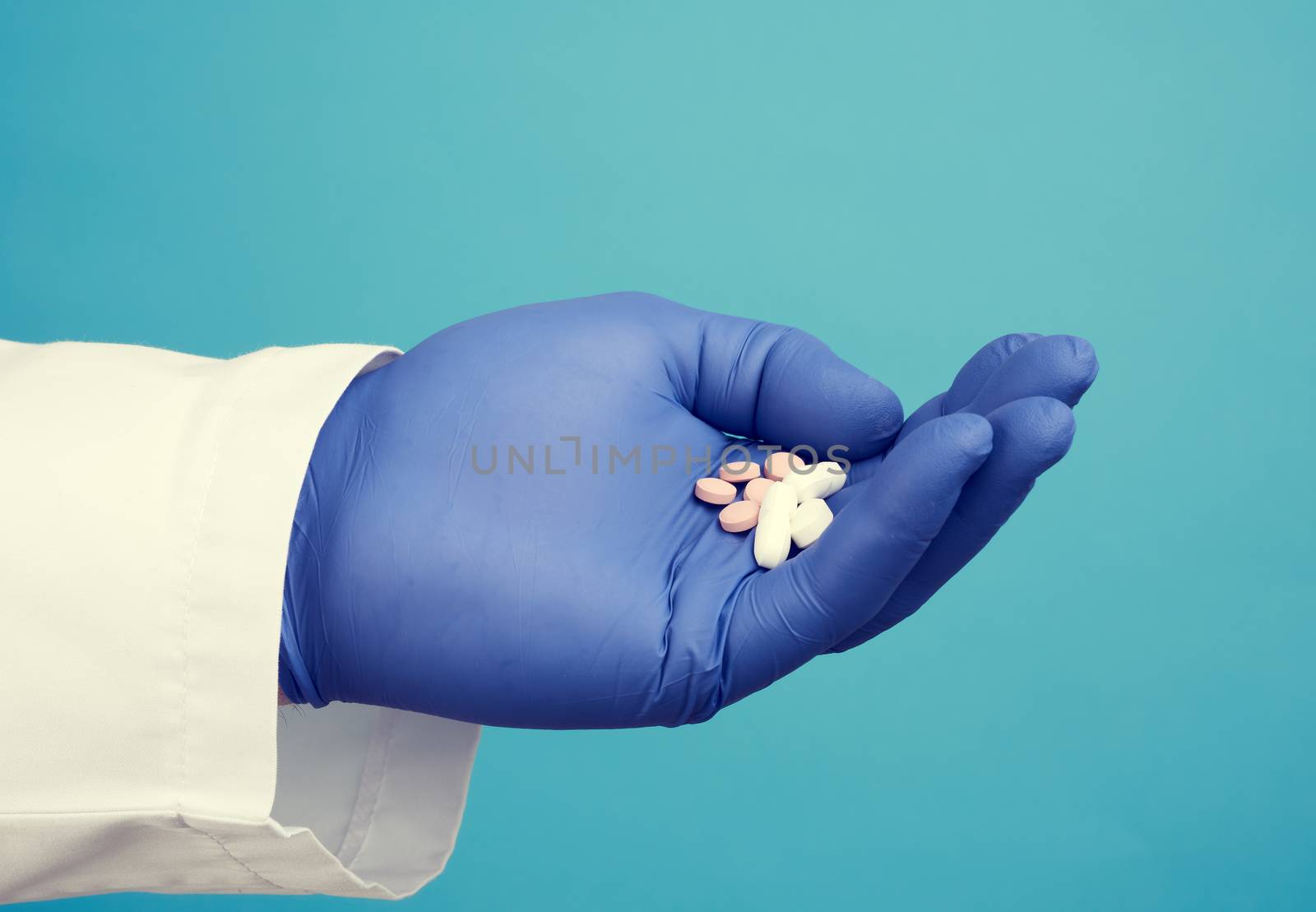 male hand with blue sterile gloves holds white pills, concept of drug treatment for diseases, blue background