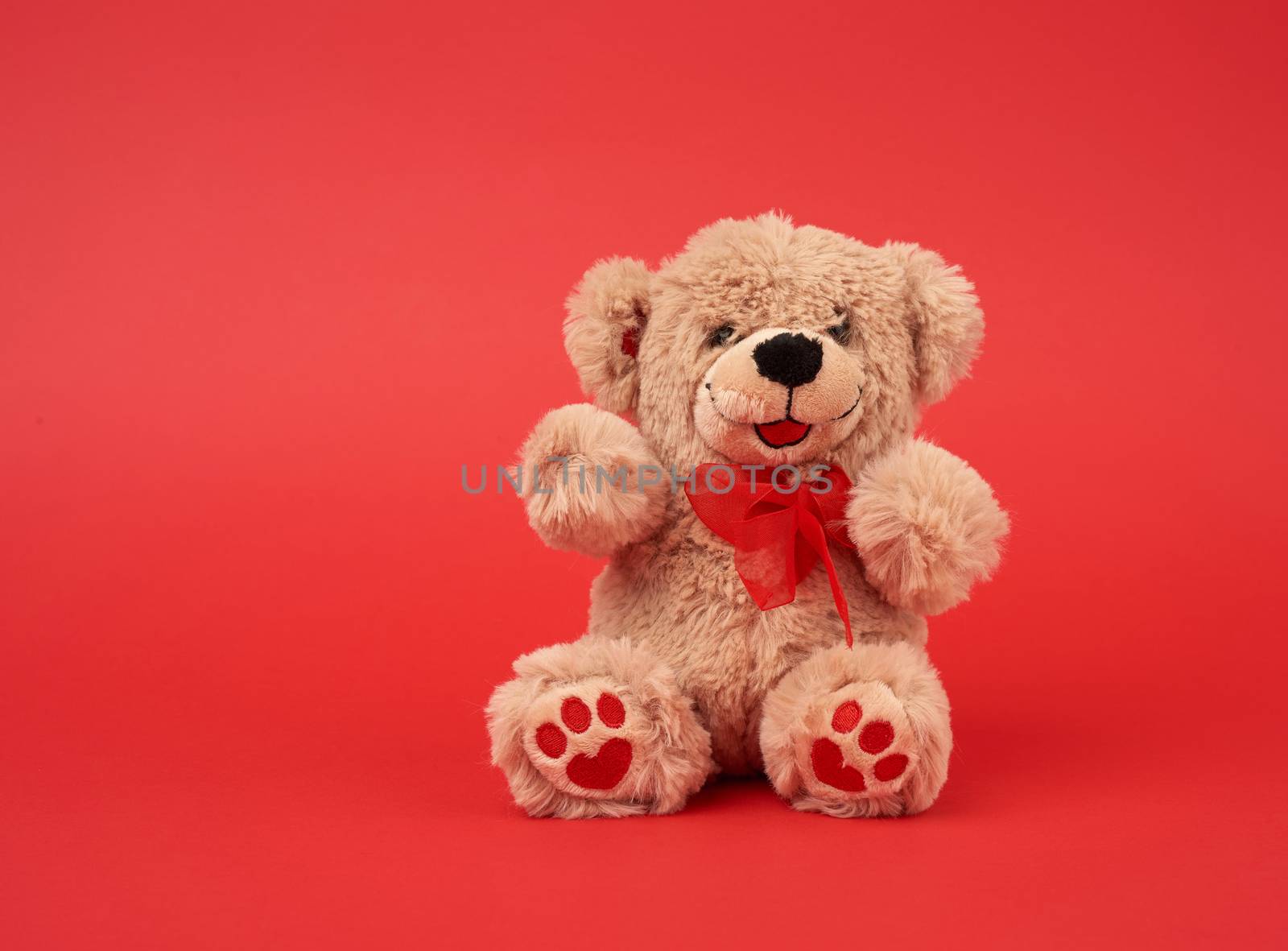 cute little brown teddy bear, toy is sitting on a red background, close up, copy space