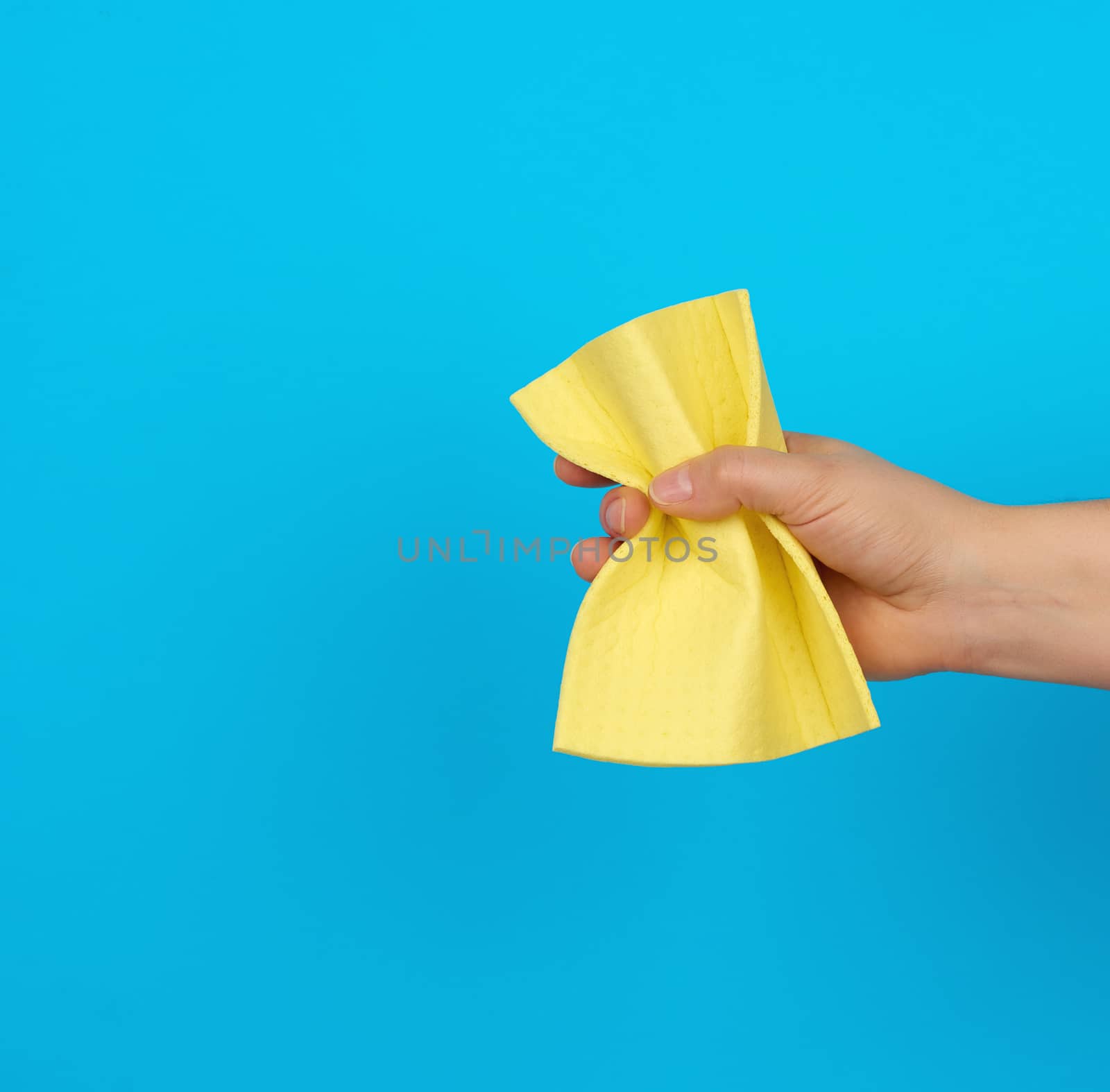 female hand holds a yellow rag sponge for cleaning, blue background