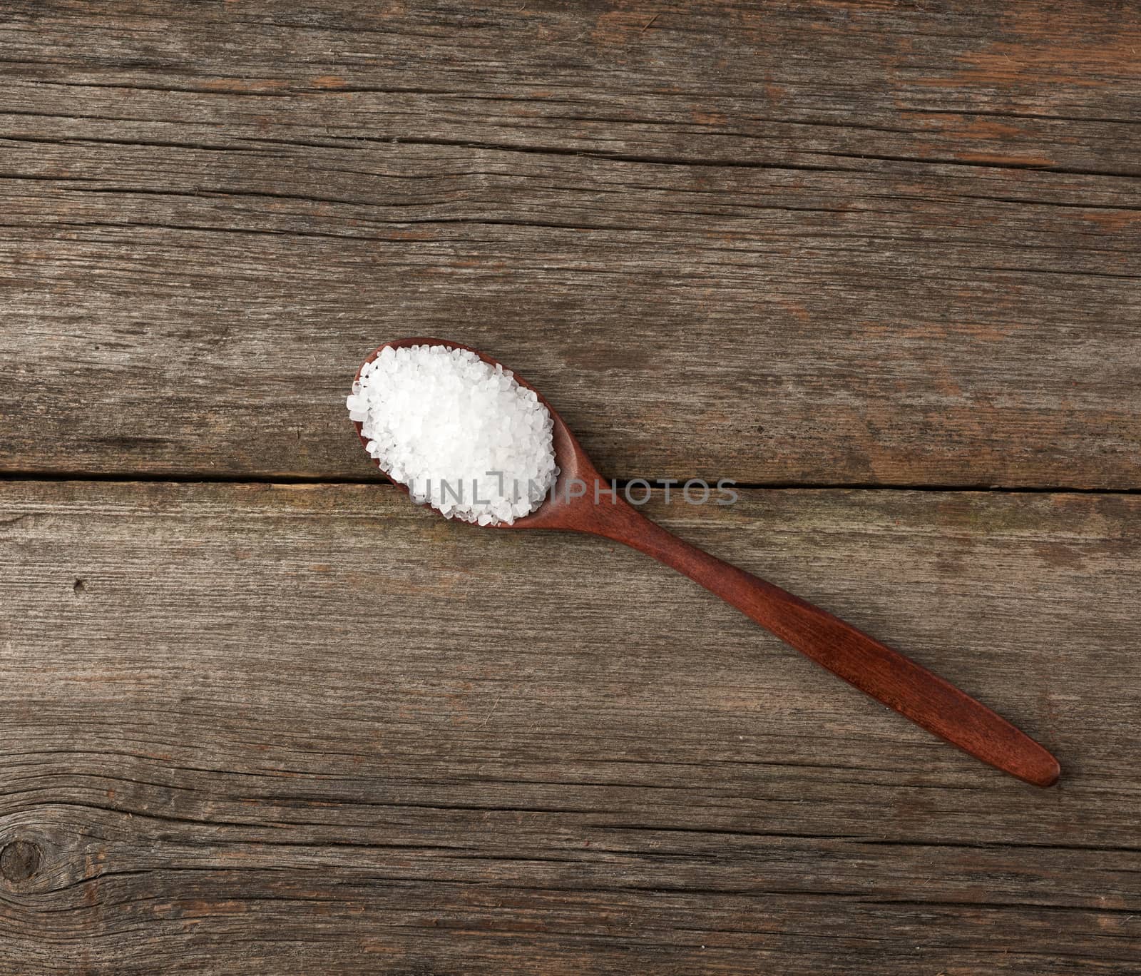 white coarse salt in a wooden spoon, gray table from old boards, top view