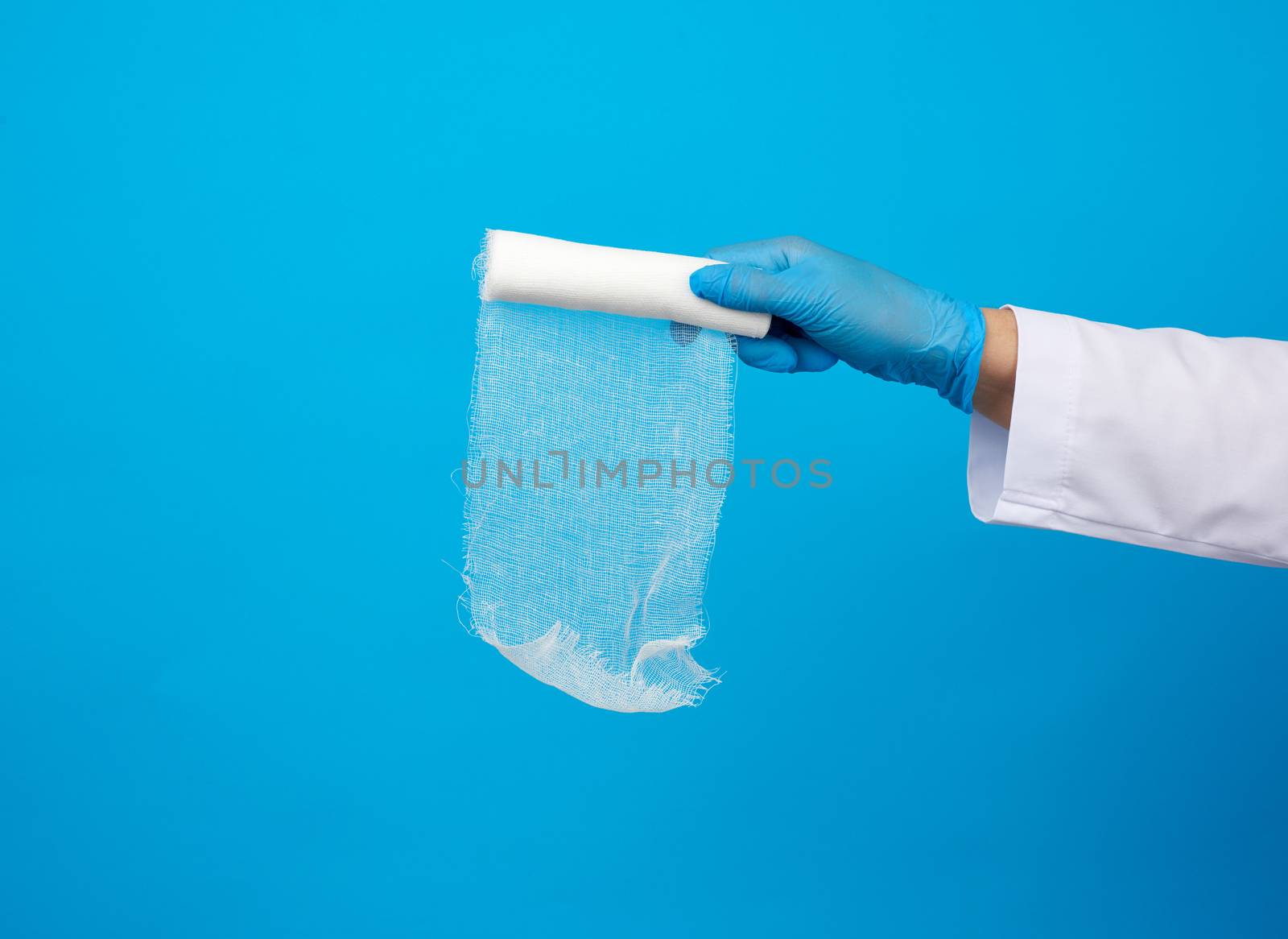 medic woman in white coat holds a twisted gauze bandage for dressing wounds, blue background