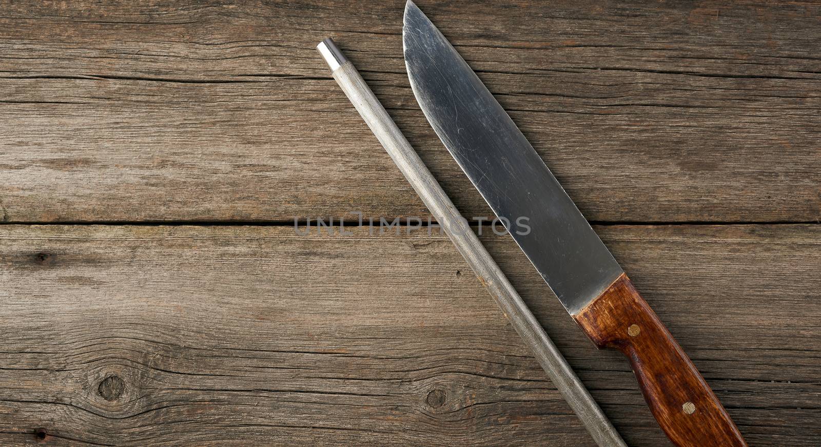 knife and old iron sharpener with handle for kitchen knives on gray wooden background, top view, copy space