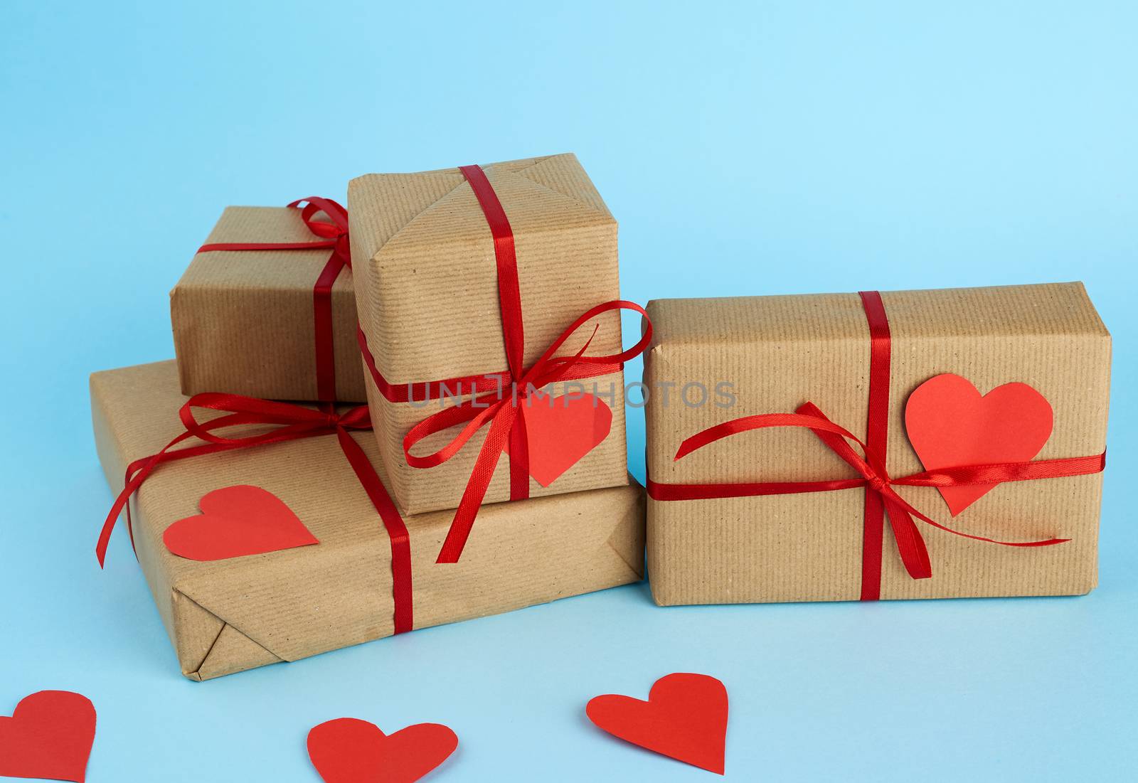 stack of wrapped gifts in brown kraft paper and tied with a red ribbon on a blue background, surprise and a gift for Valentine's Day February 14