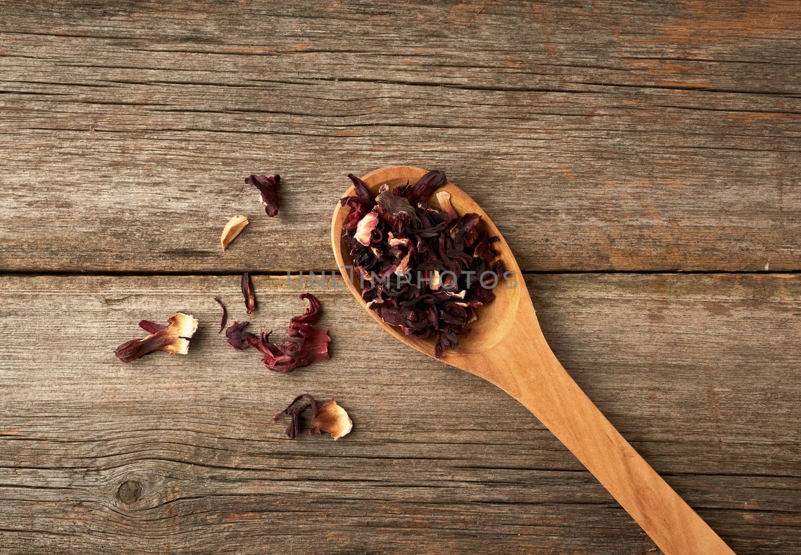 dry petals of red hibiscus in a wooden spoon, tea preparation, top view