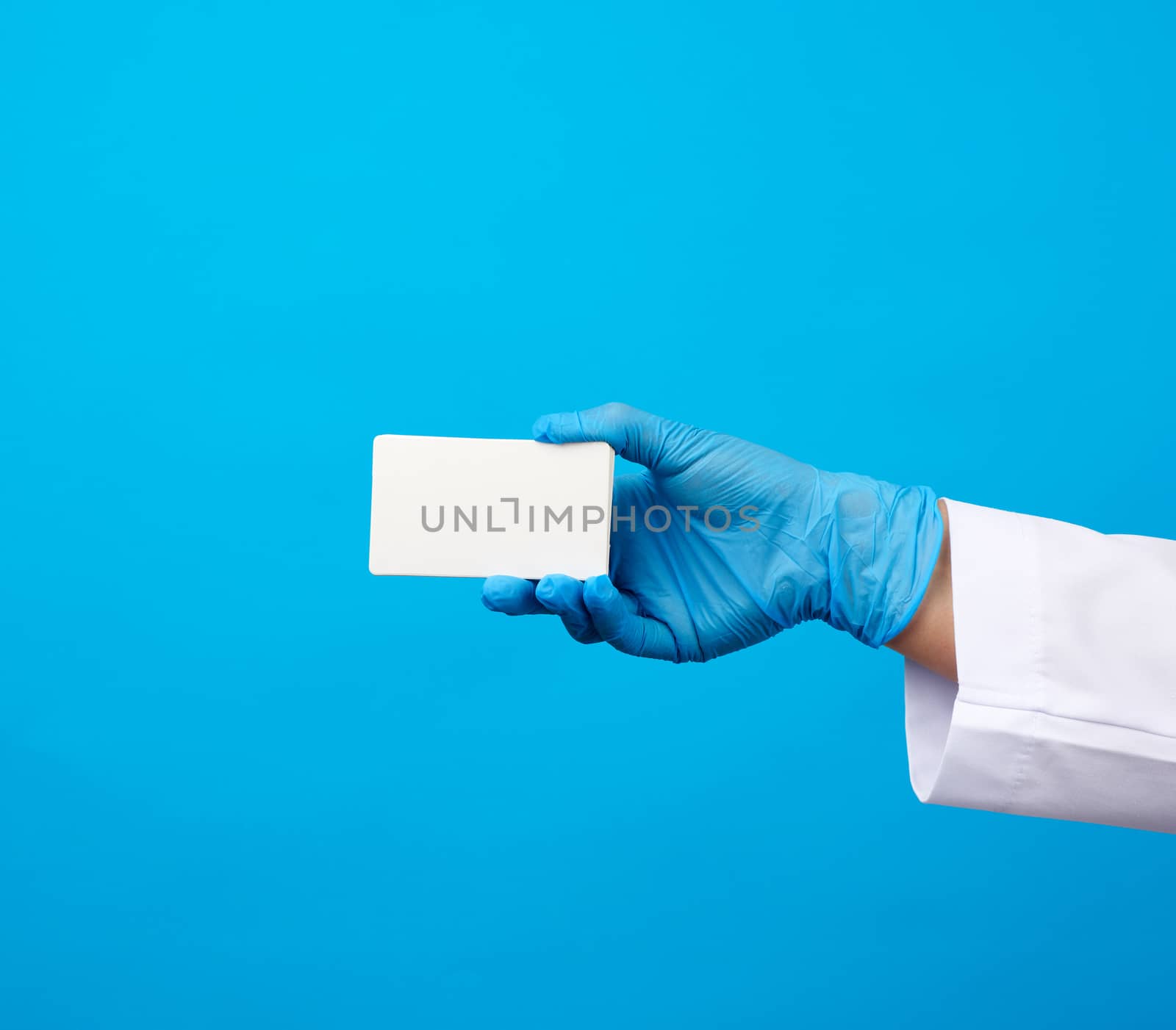 female doctor hand in blue medical latex gloves holds an empty paper business card on a blue background, place for an inscription