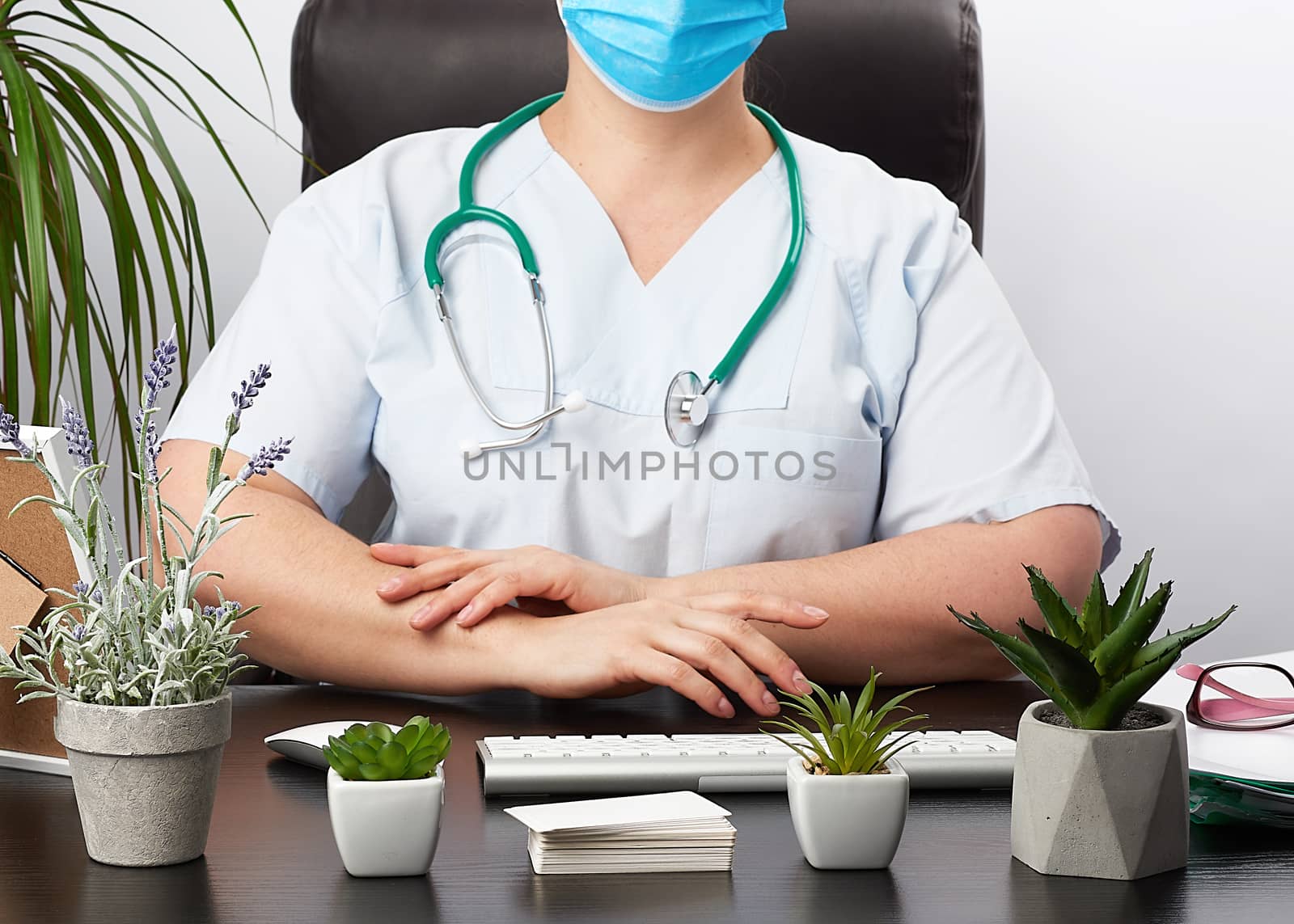doctor gloves sits at a white work table in his office, concept of patient reception in the clinic, hands joined in front of the chest, focused pose