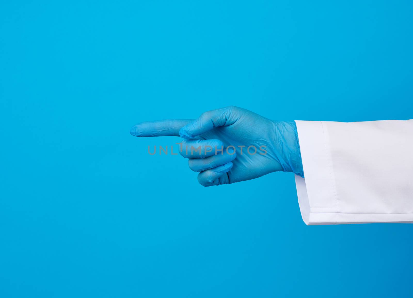 medic woman in white coat, wearing in blue sterile gloves, showing hand gesture indicating the subject, blue background
